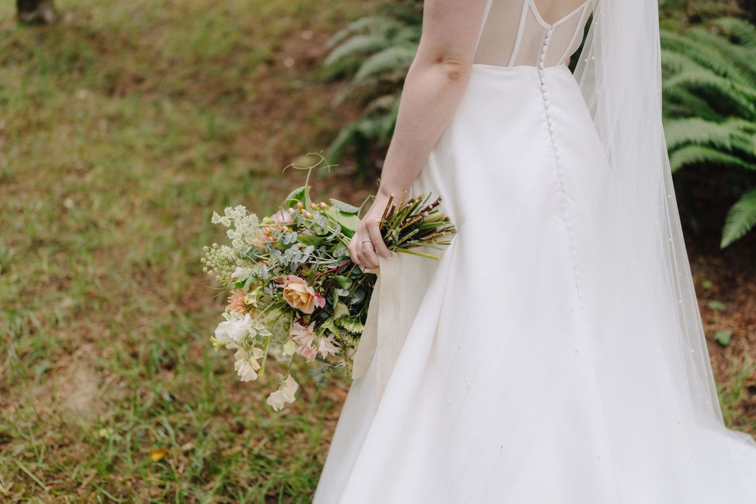 Flowing white wedding dress details with delicate lace and tulle against natural outdoor backdrop.