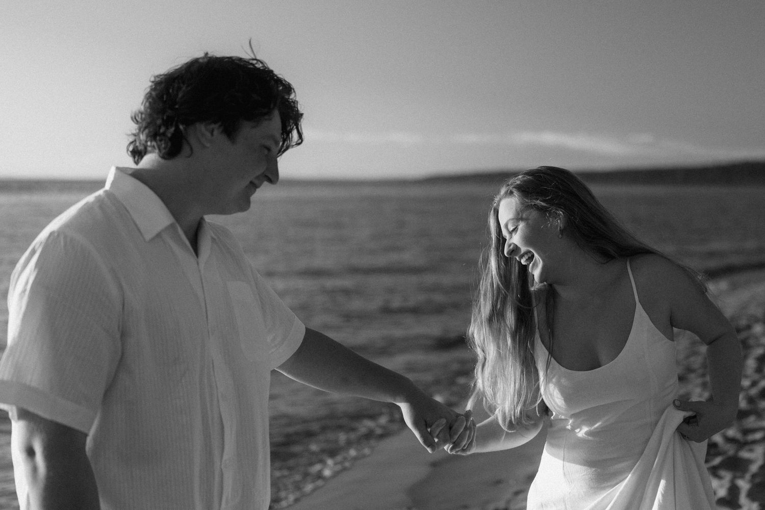 A joyful couple sharing a candid moment together on the beach in black and white photography.
