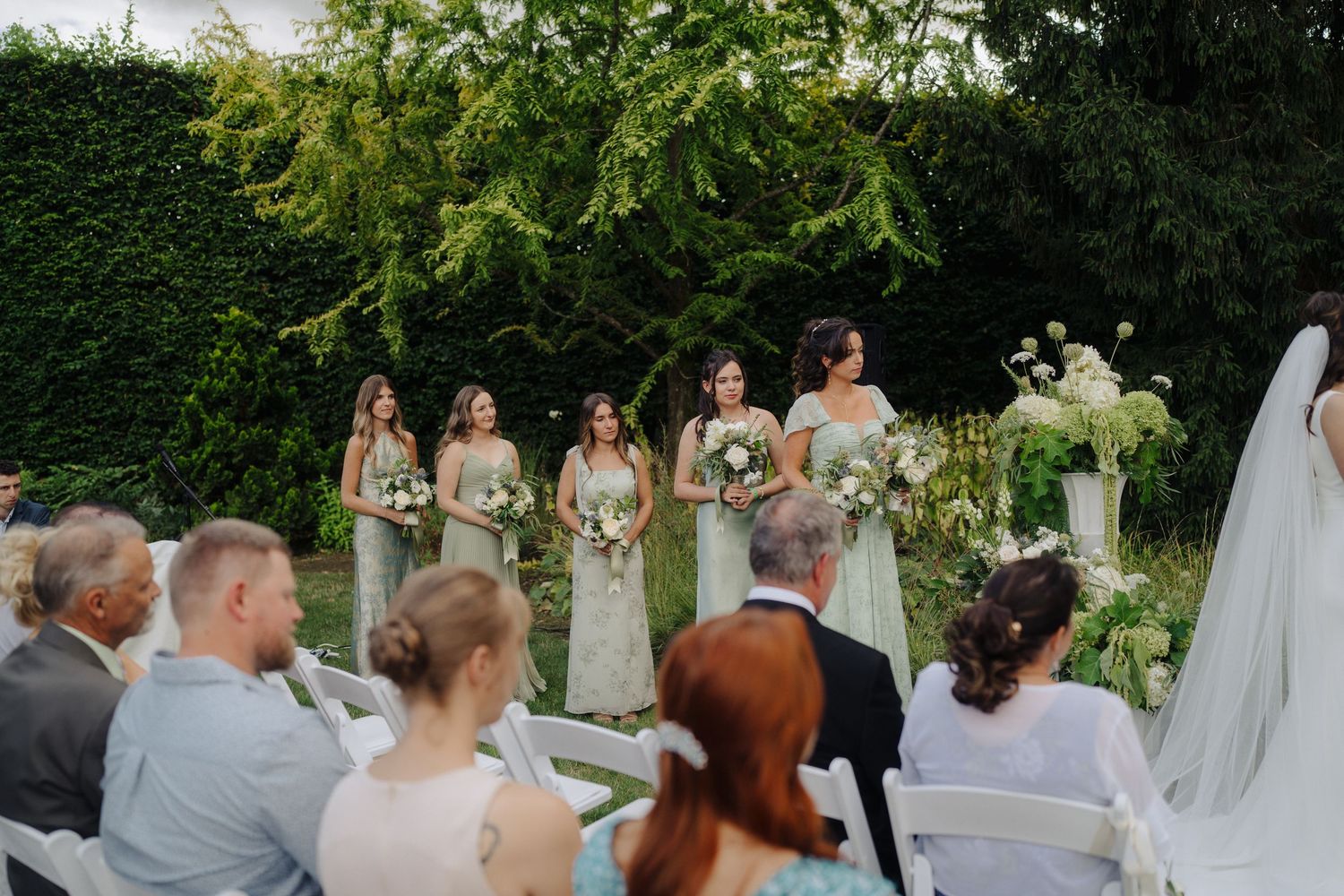 Wedding ceremony setup in an outdoor garden with white chairs and floral arrangements.