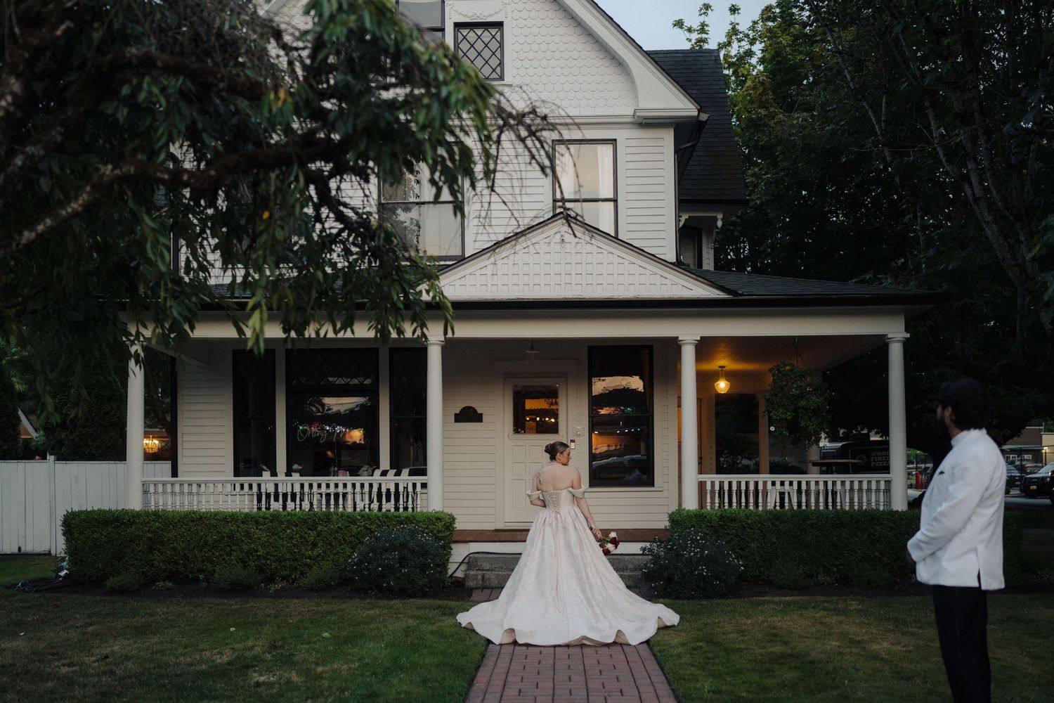 White farmhouse style venue with wrap-around porch and elegant landscaping for an outdoor wedding celebration.