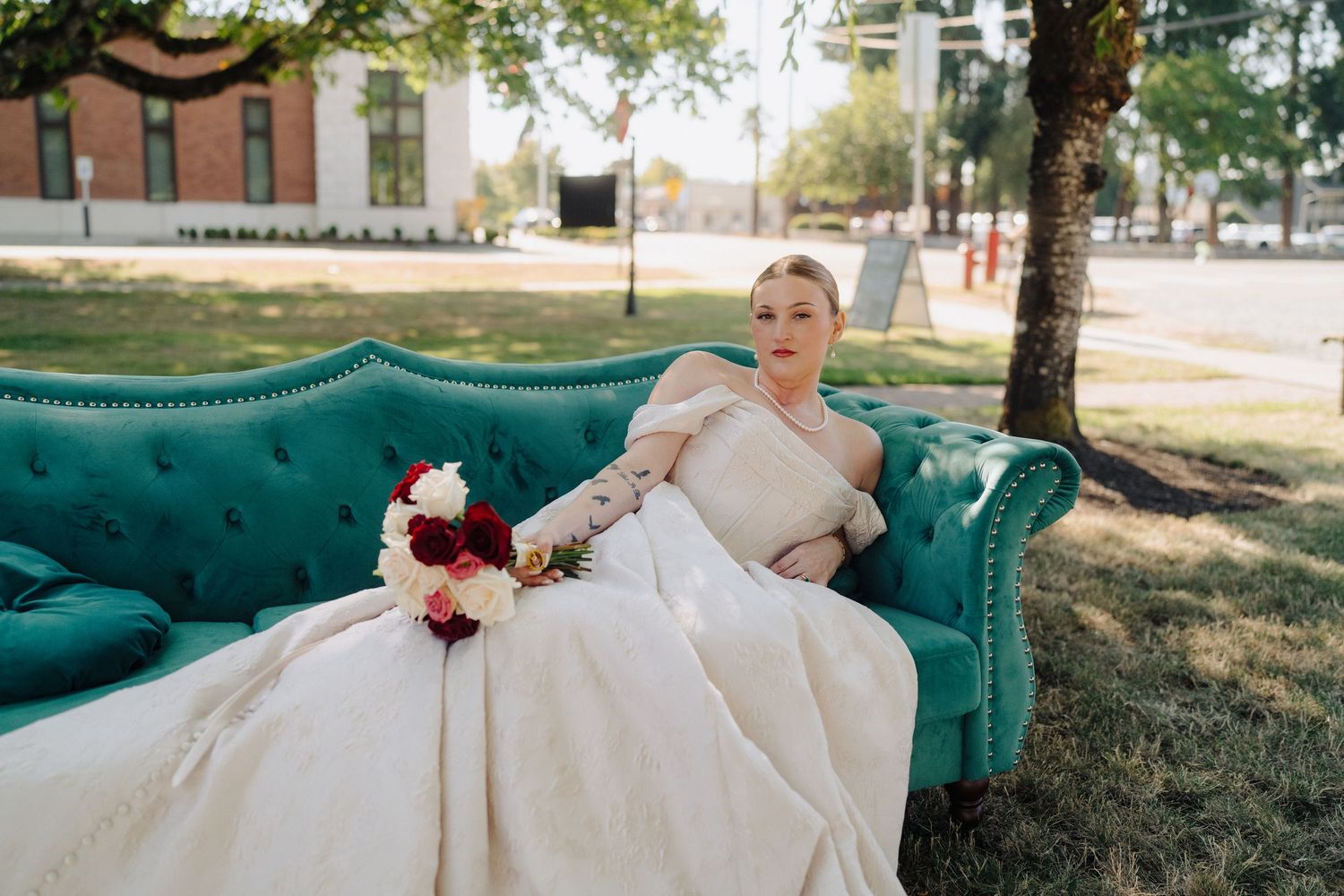 Elegant wedding dress flows across teal vintage couch in outdoor garden setting.