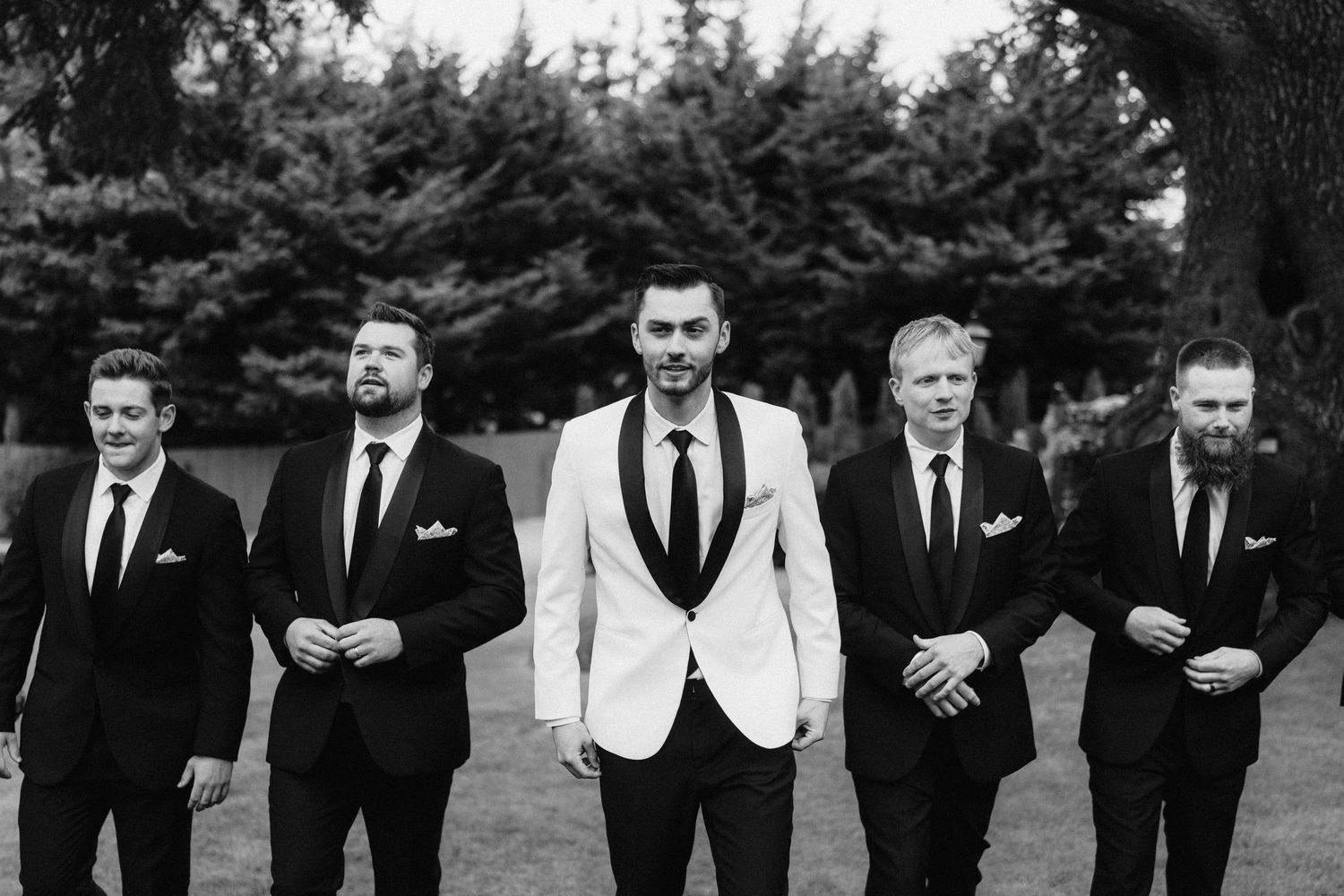 A black and white panoramic photo shows a wedding party in formal attire standing together outdoors.