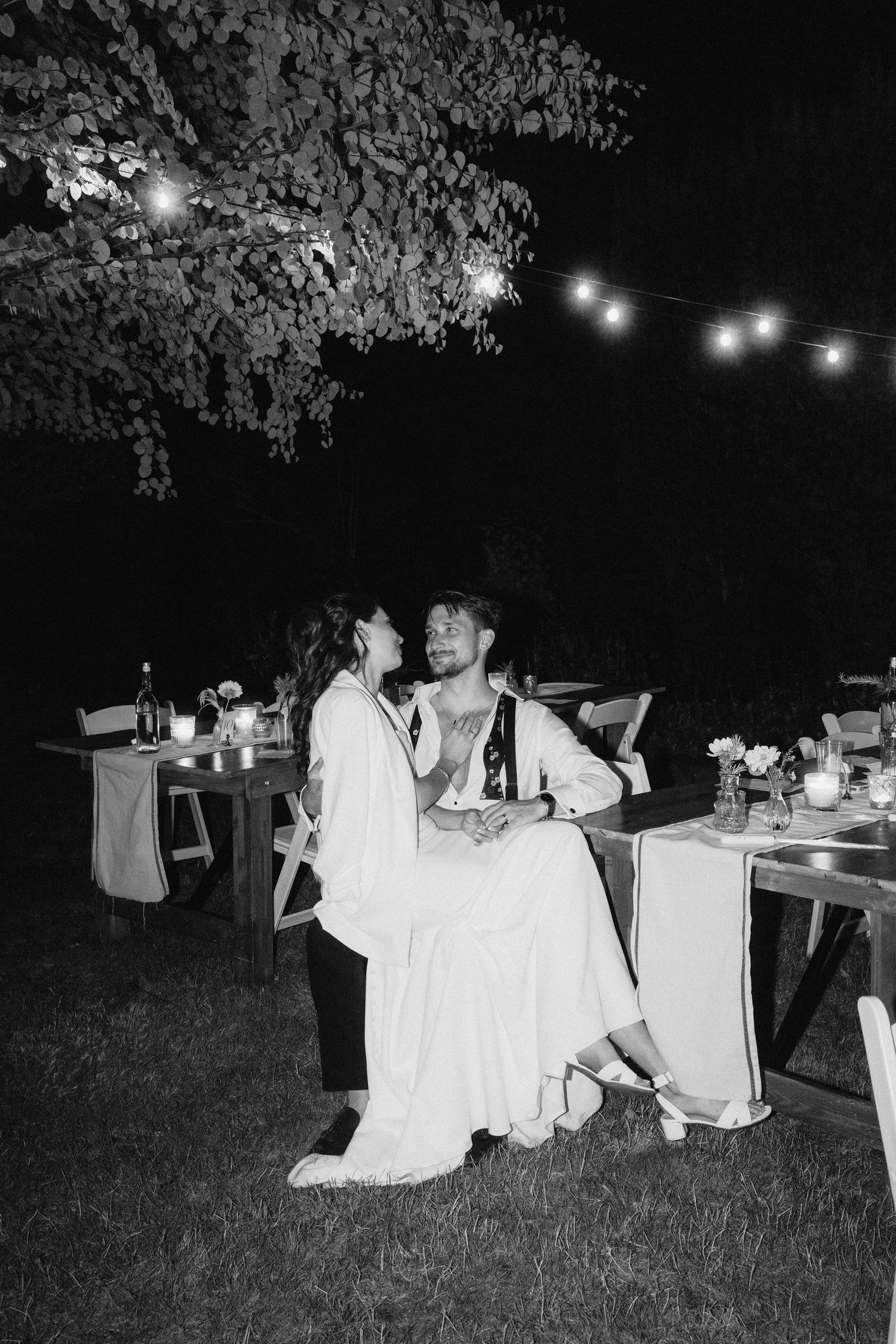 An outdoor evening reception with string lights and white tablecloths creates an intimate atmosphere.
