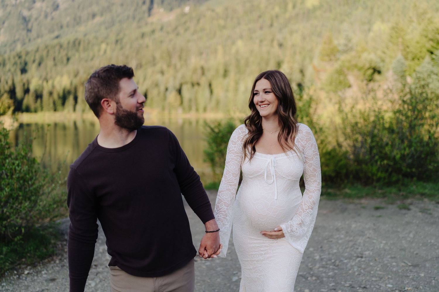 Couple sharing an intimate moment on a lakeshore with mountains and forest in the background.