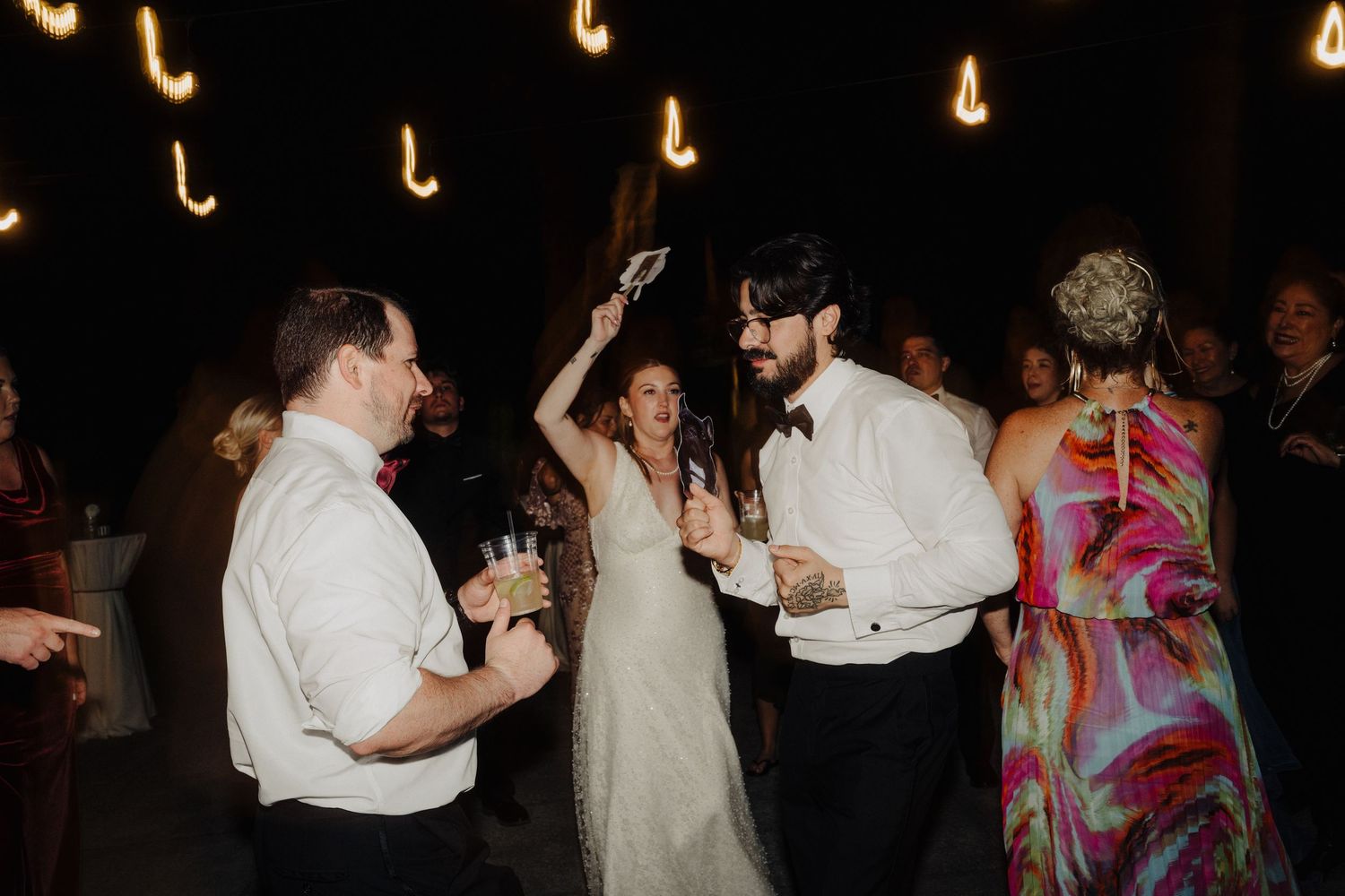 Couples dancing together at a dimly lit reception with warm glowing lights in the background.