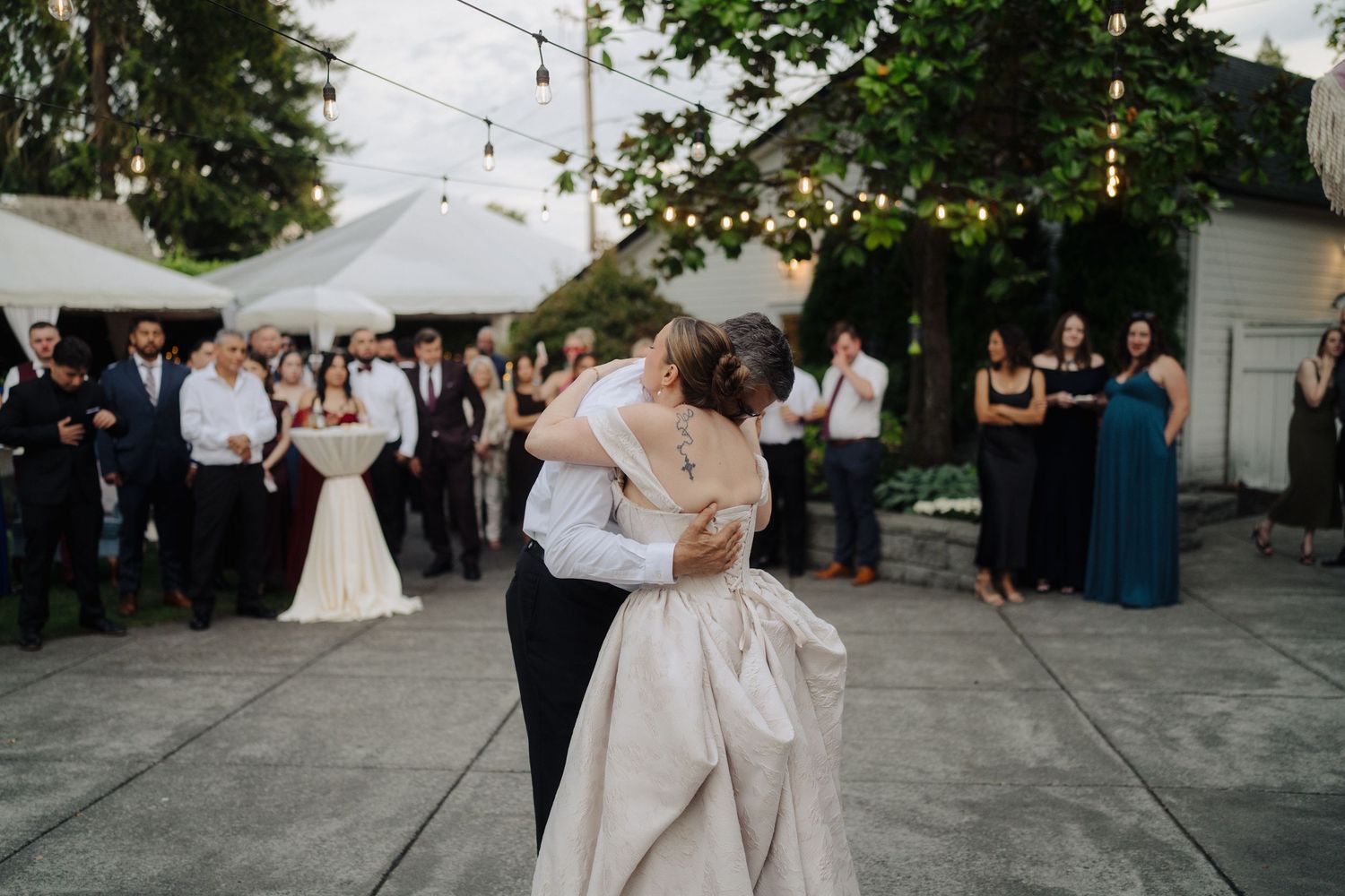 Wedding guests dancing and celebrating on an outdoor patio under string lights.