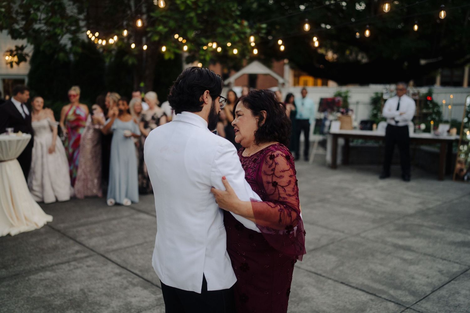 Couples dancing at twilight wedding reception on outdoor patio with string lighting.