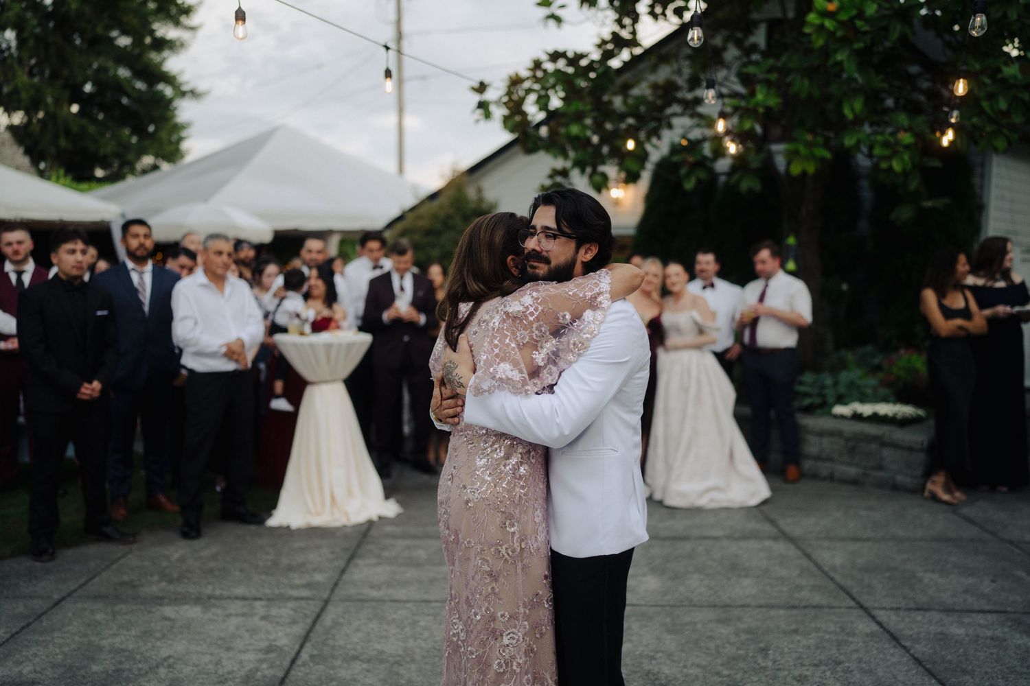 Couples dancing together on outdoor patio under string lights at wedding reception.