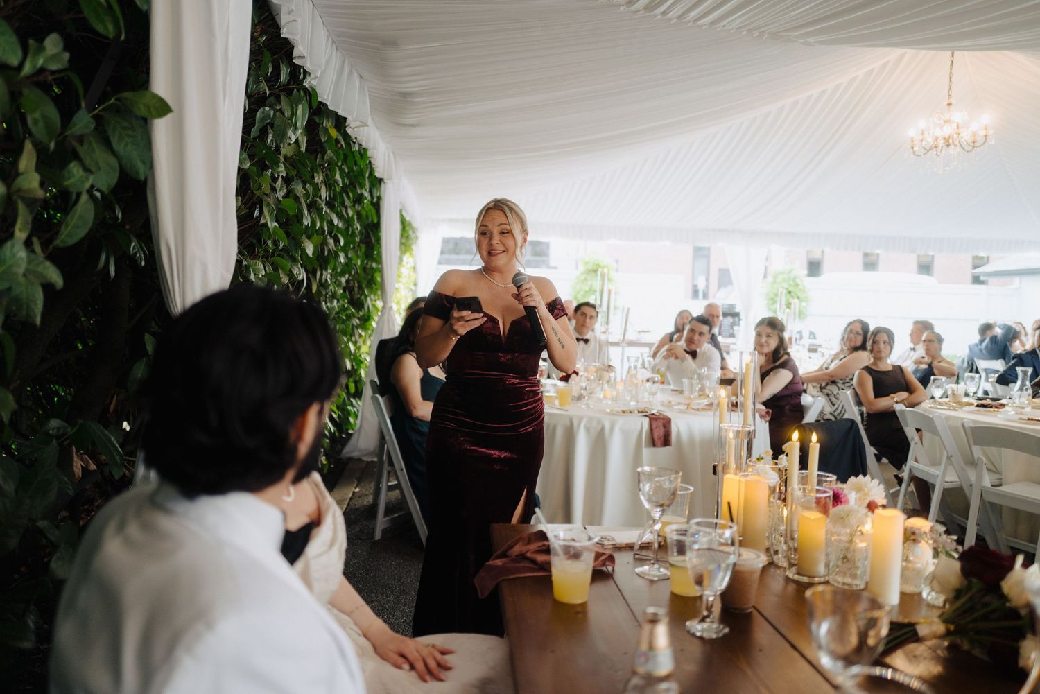 Elegant wedding reception table settings with white linens and candlelight under draped ceiling.