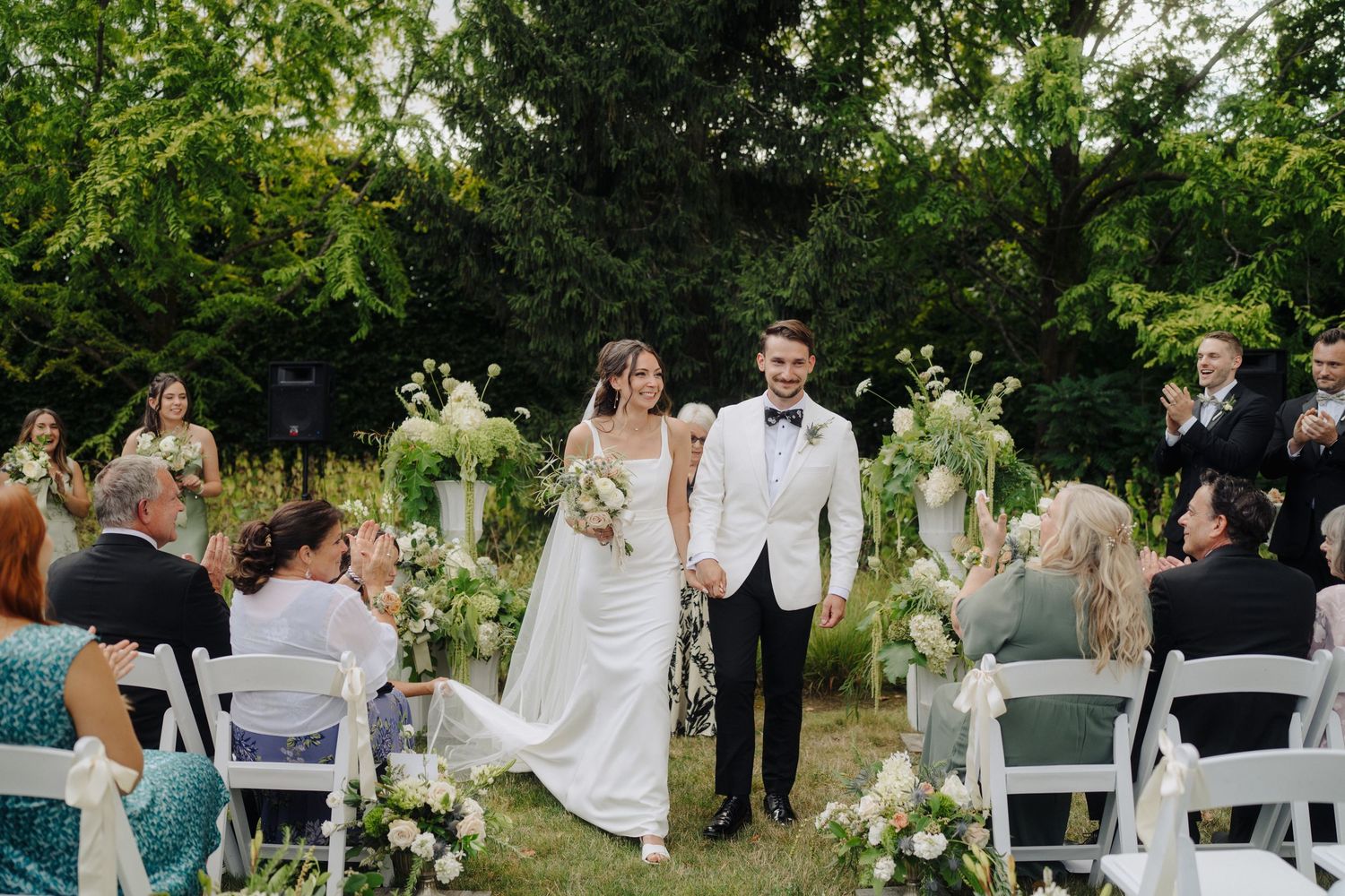 Outdoor wedding ceremony with white chairs set up in a garden setting.