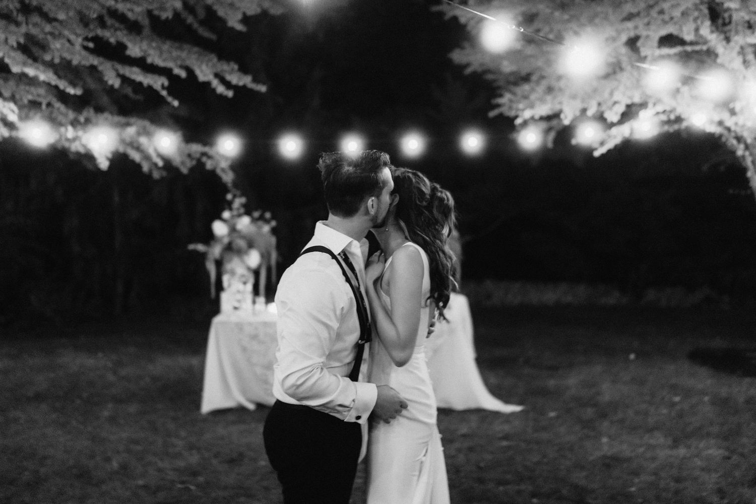 String lights twinkle above a romantic outdoor wedding celebration at dusk.