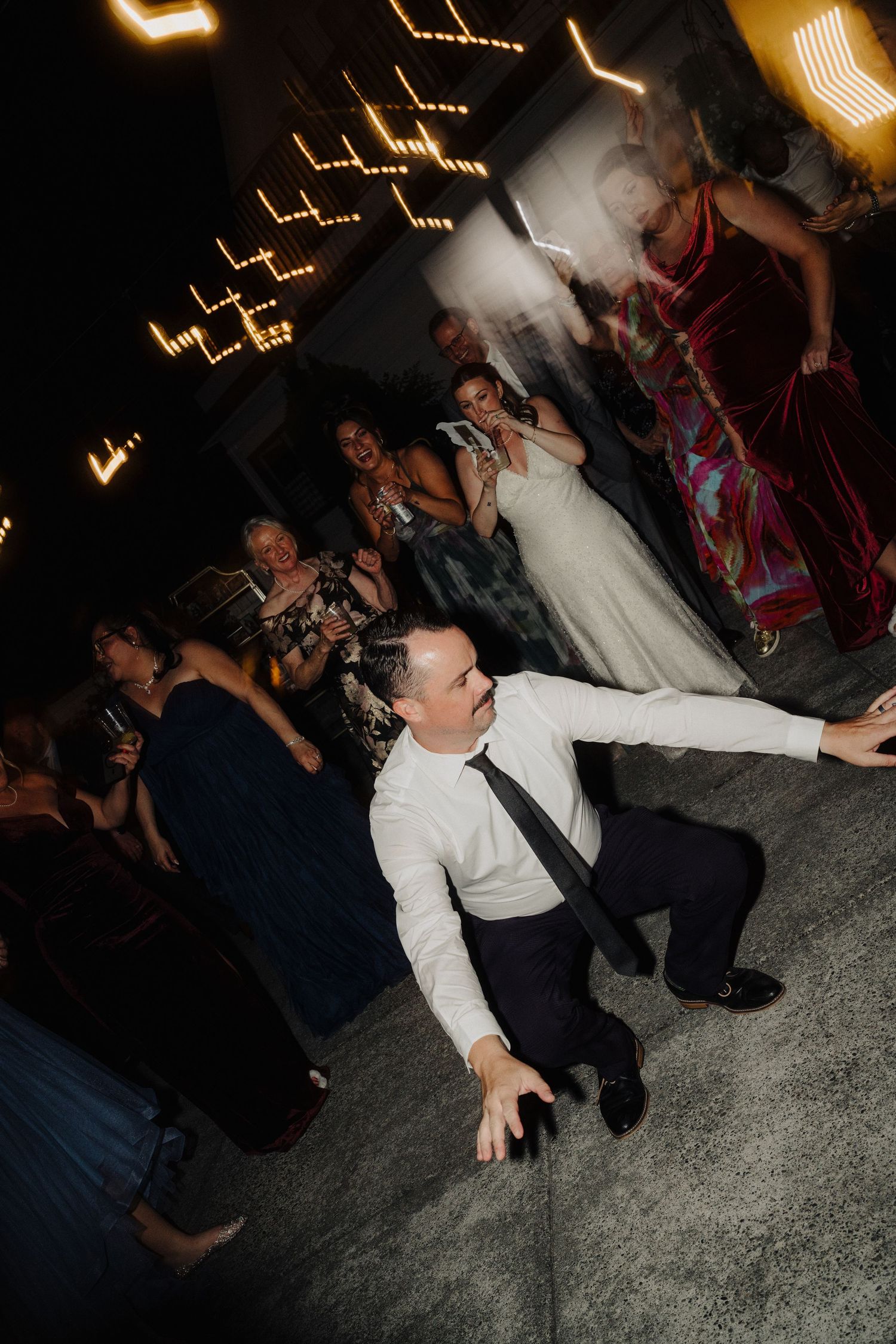 Wedding reception guests dancing energetically on a dark dance floor with illuminated decor.