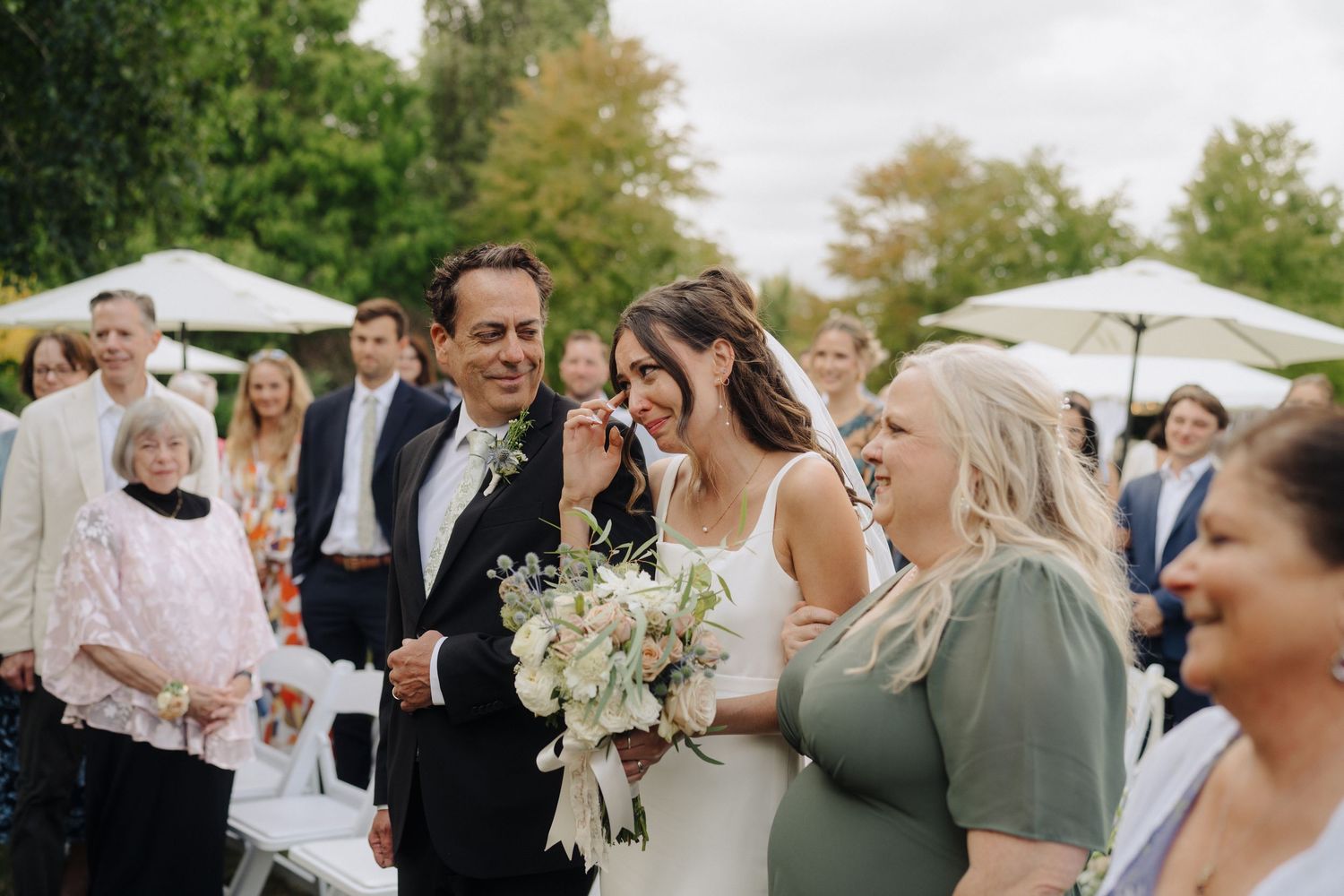 Wedding guests gather outdoors under white umbrellas during a summer celebration.