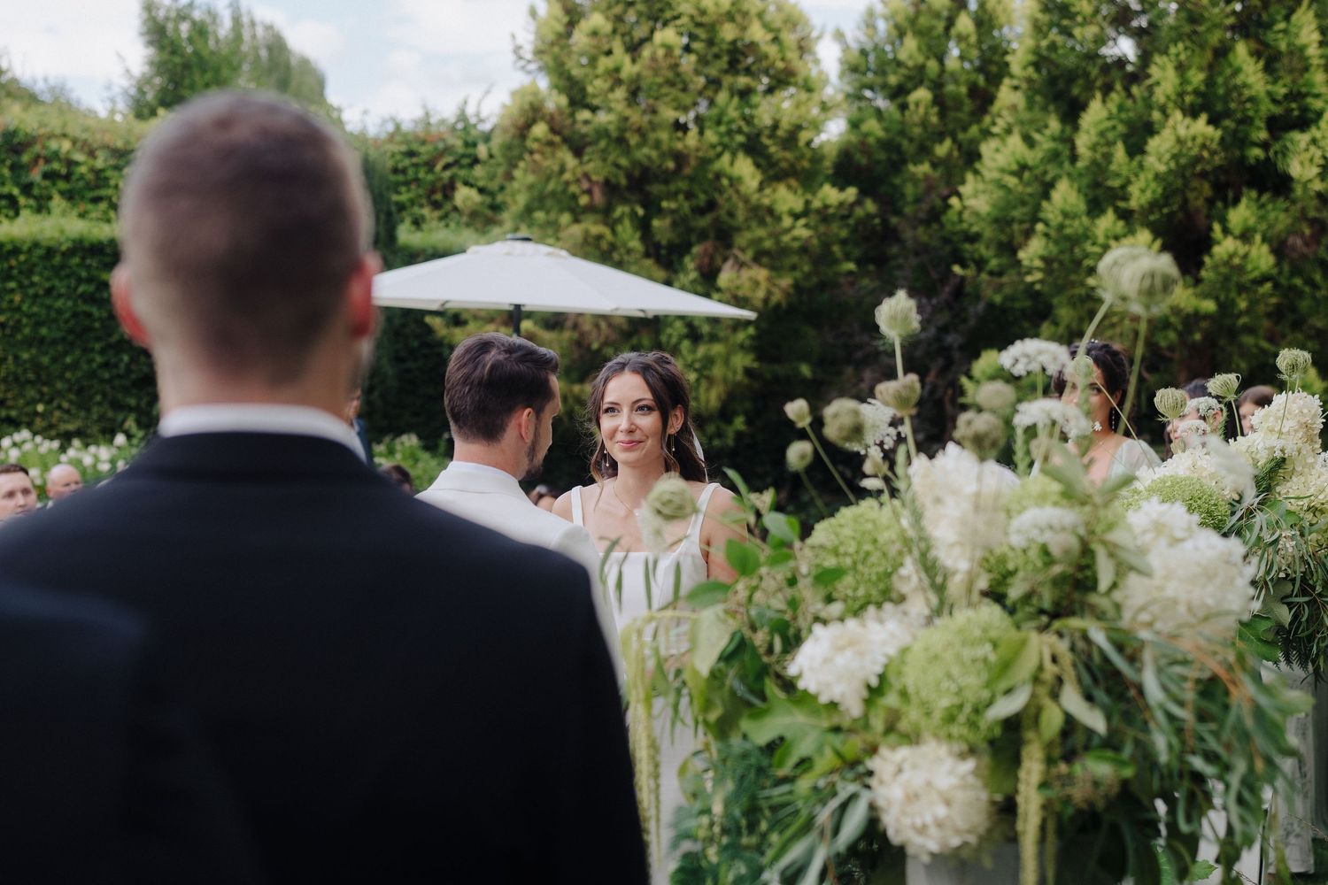 Elegant outdoor wedding ceremony with white floral arrangements and garden backdrop.