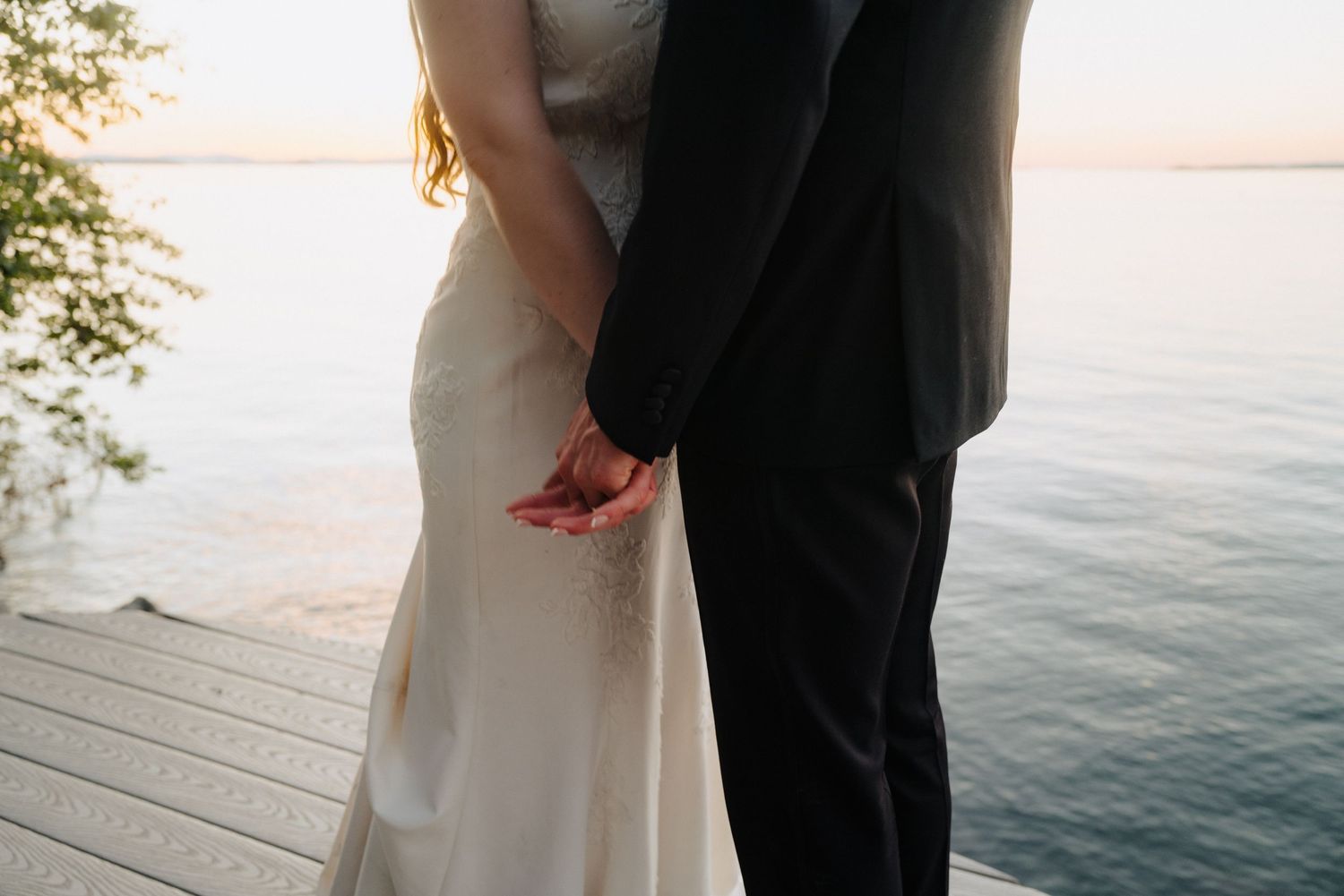 Couple stands together against waterfront backdrop during sunset.