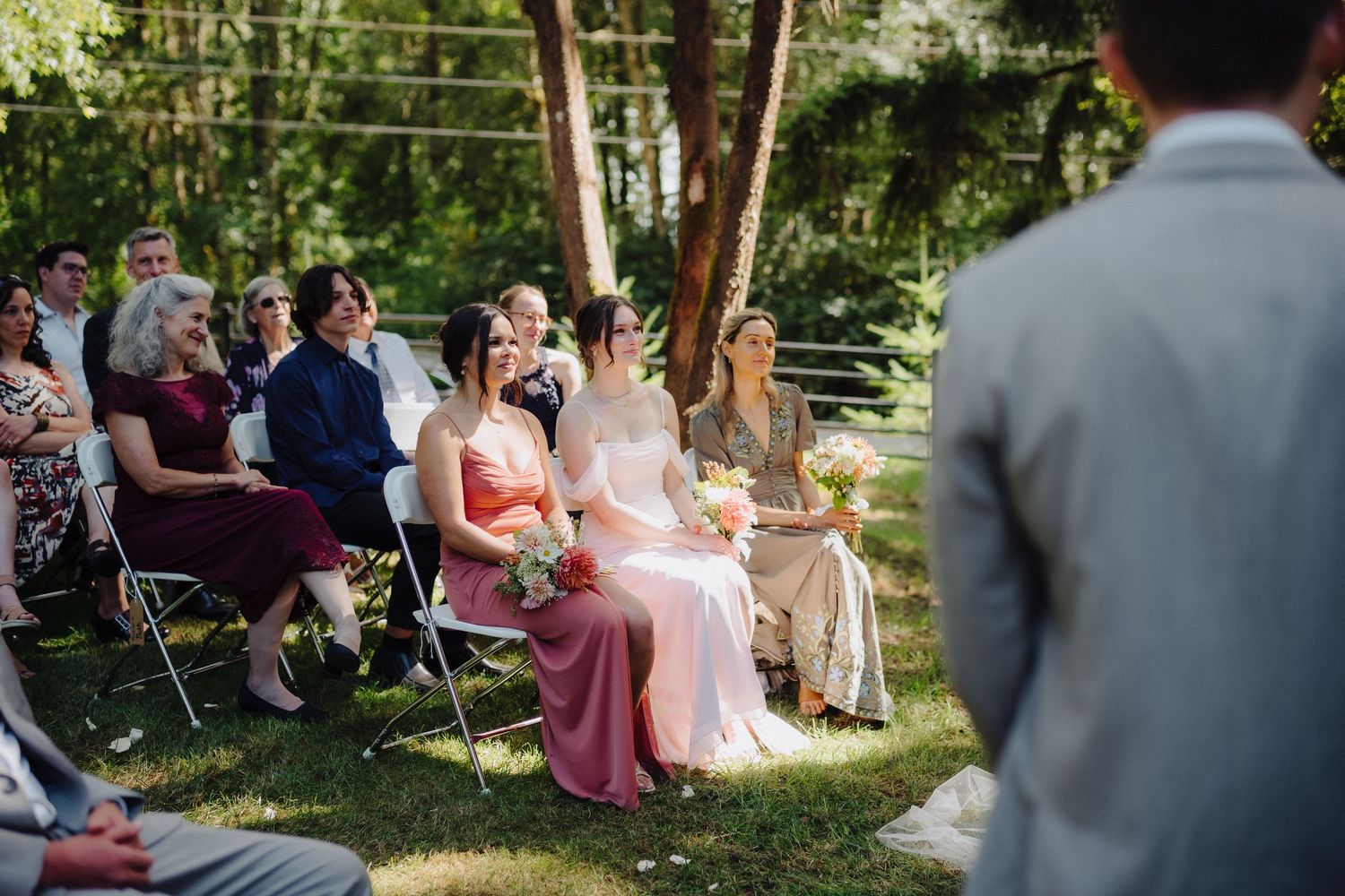 Wedding guests seated outdoors in chairs on a lawn during a summer garden ceremony.