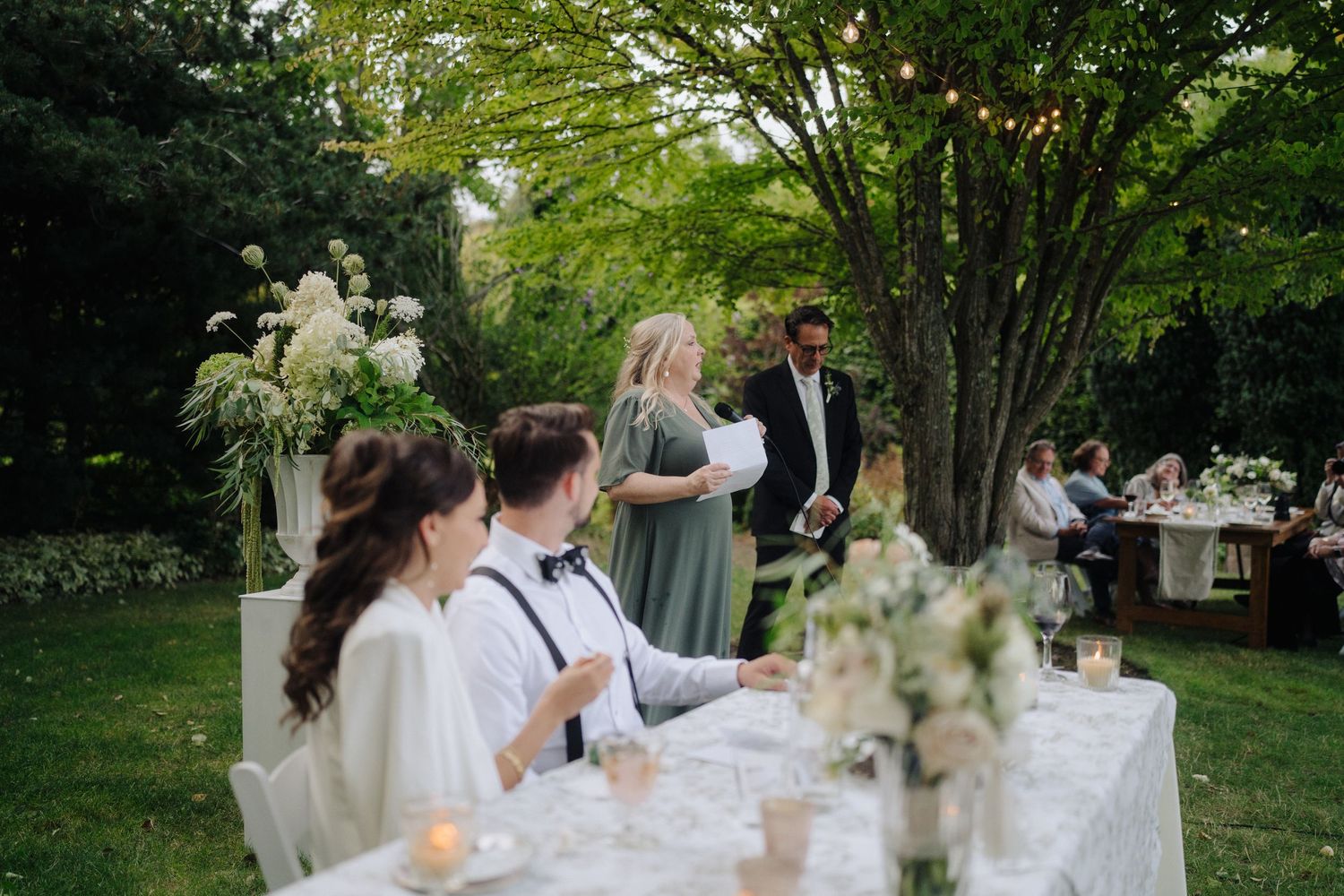 Wedding guests mingling at an outdoor reception with white-clothed tables.