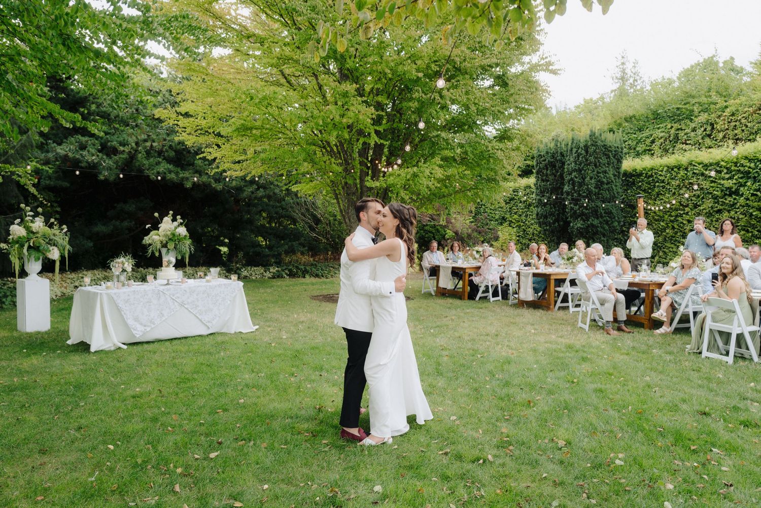 Outdoor wedding reception scene with guests seated in a natural garden setting.
