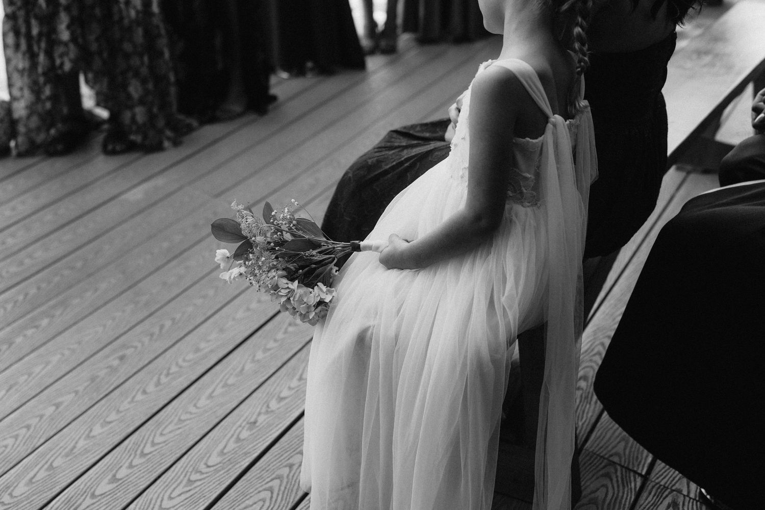 Black and white photo of a flowing white wedding dress on a wooden deck during a ceremony.