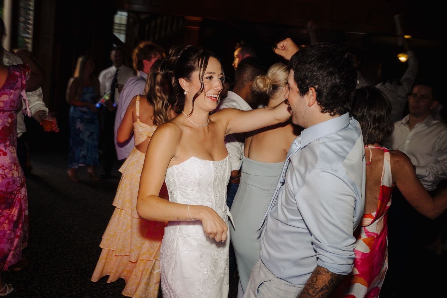 Wedding reception dance floor filled with guests celebrating in dimly lit venue.