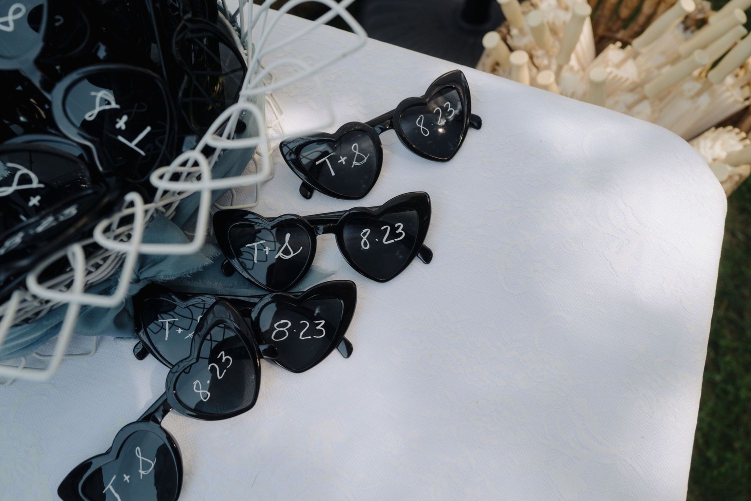 Black heart-shaped sunglasses with dates written on them displayed on white surface.
