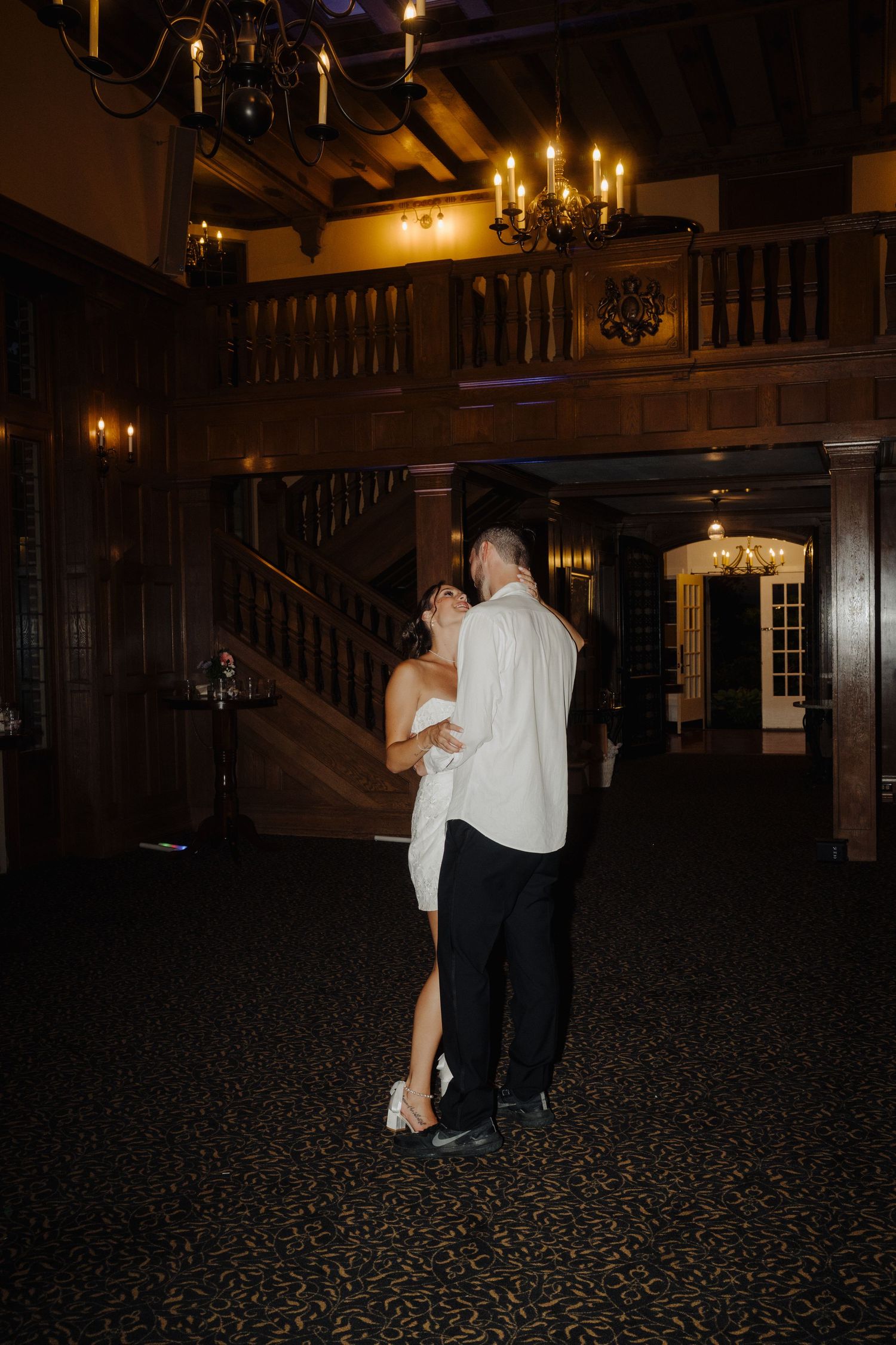 Couple dancing in a dimly lit ballroom with wooden walls and candlelight.