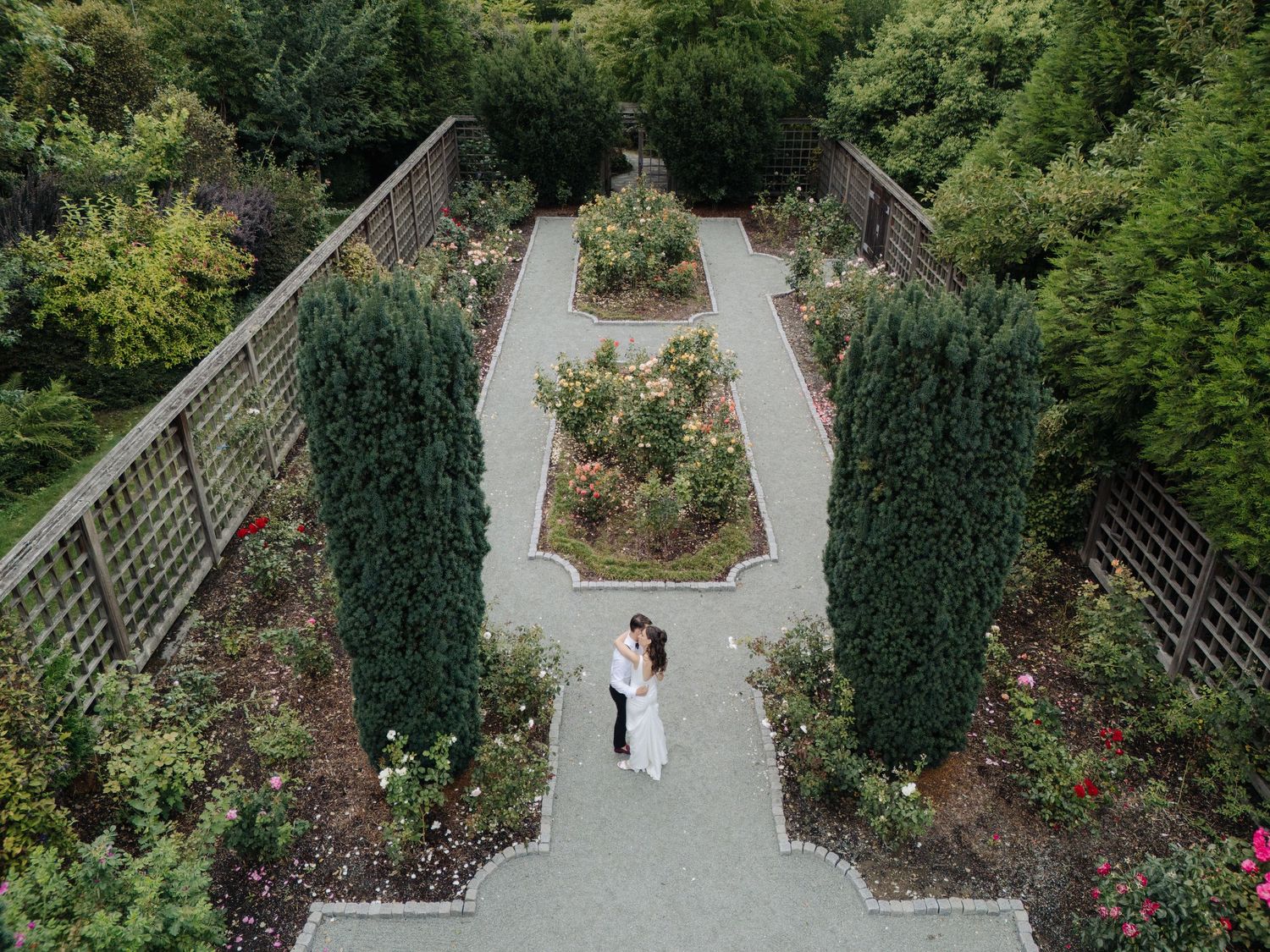 Aerial view of wedding ceremony in a formal garden with stone pathways and manicured hedges.