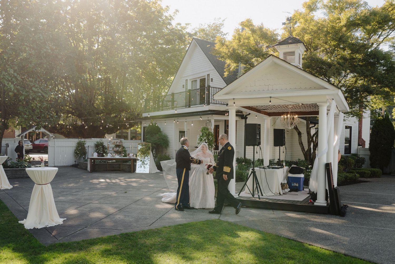 Outdoor wedding ceremony setup in front of a white house with elegant draping and cocktail tables.