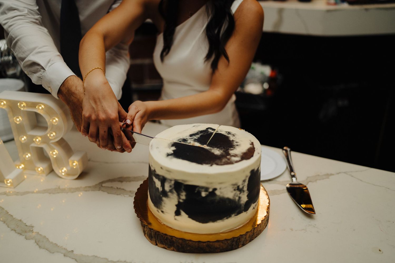 Hands cutting modern black and white wedding cake on wooden board.