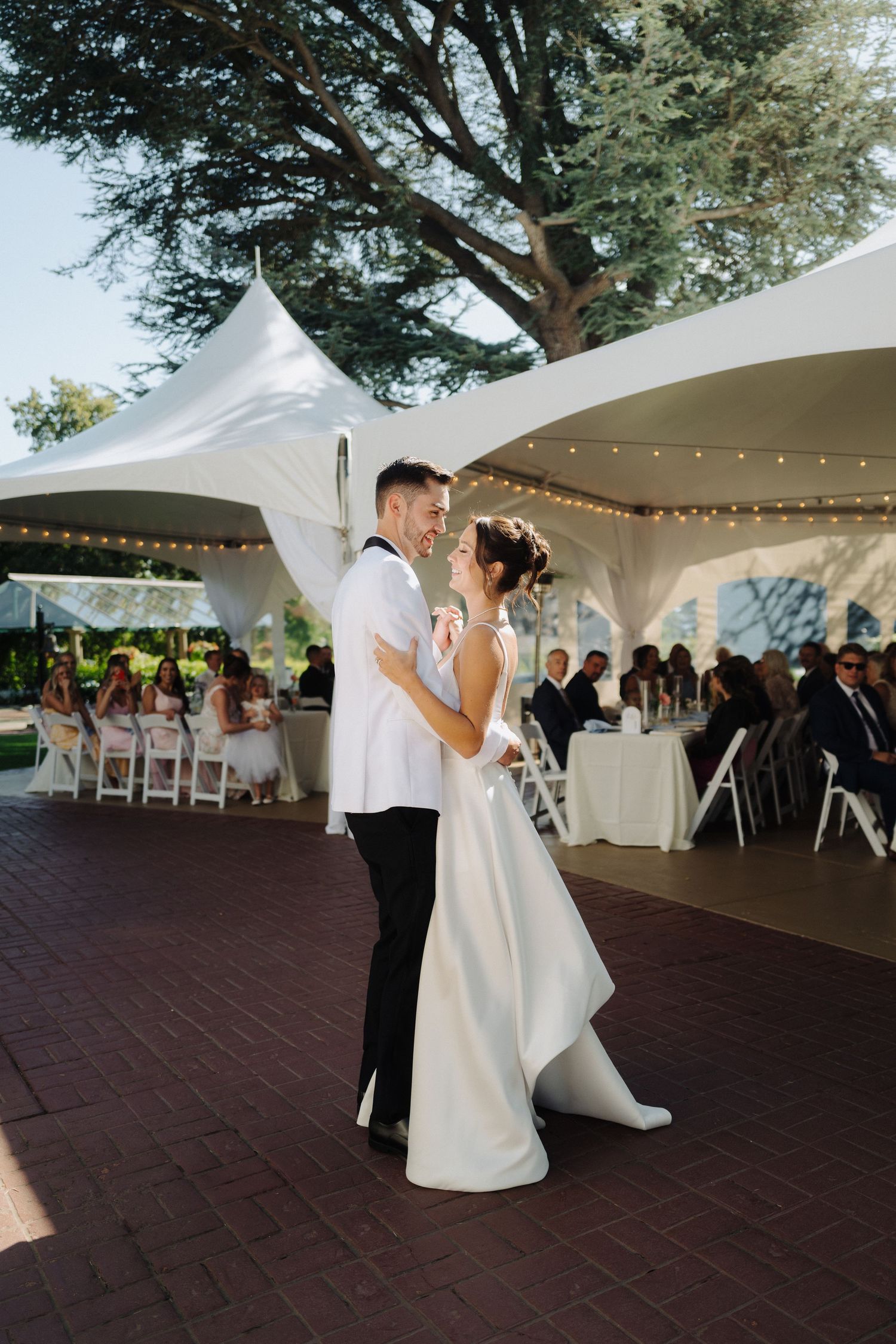 Wedding couple dances under white tent canopies during outdoor reception.