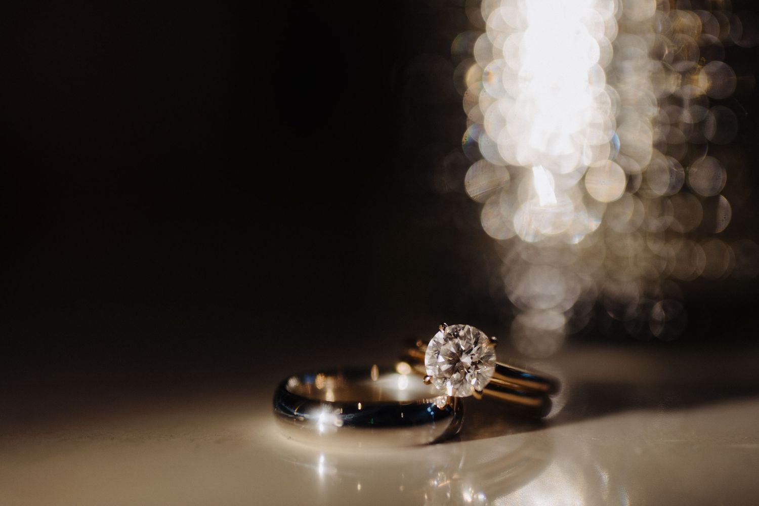 Wedding rings photographed in dramatic lighting with bokeh effects in the background.