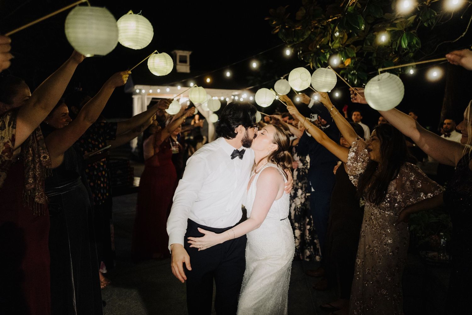 A romantic evening dance moment under glowing paper lanterns and string lights at an outdoor reception.