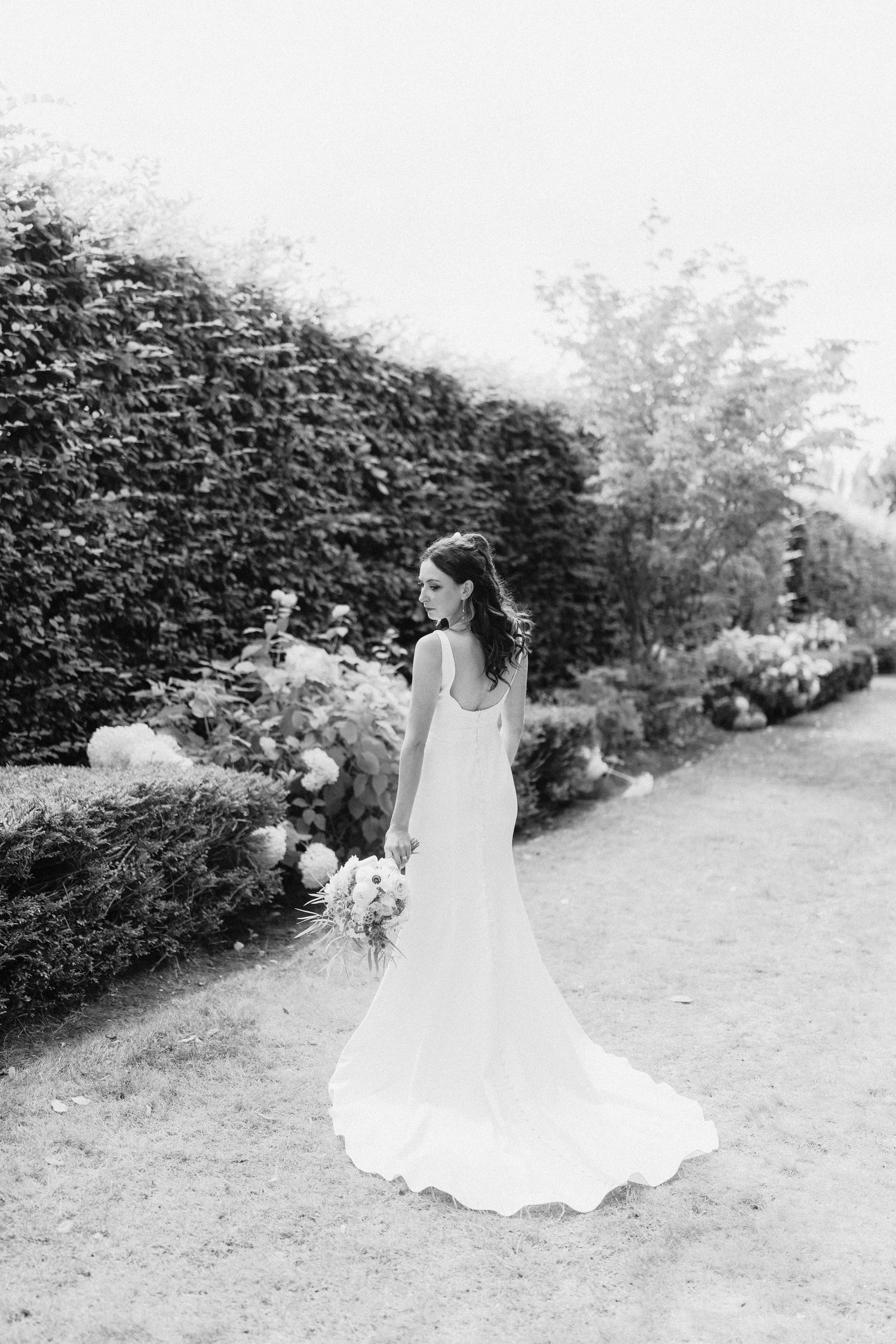 Bride in flowing white dress twirls gracefully in a garden setting captured in black and white photography.