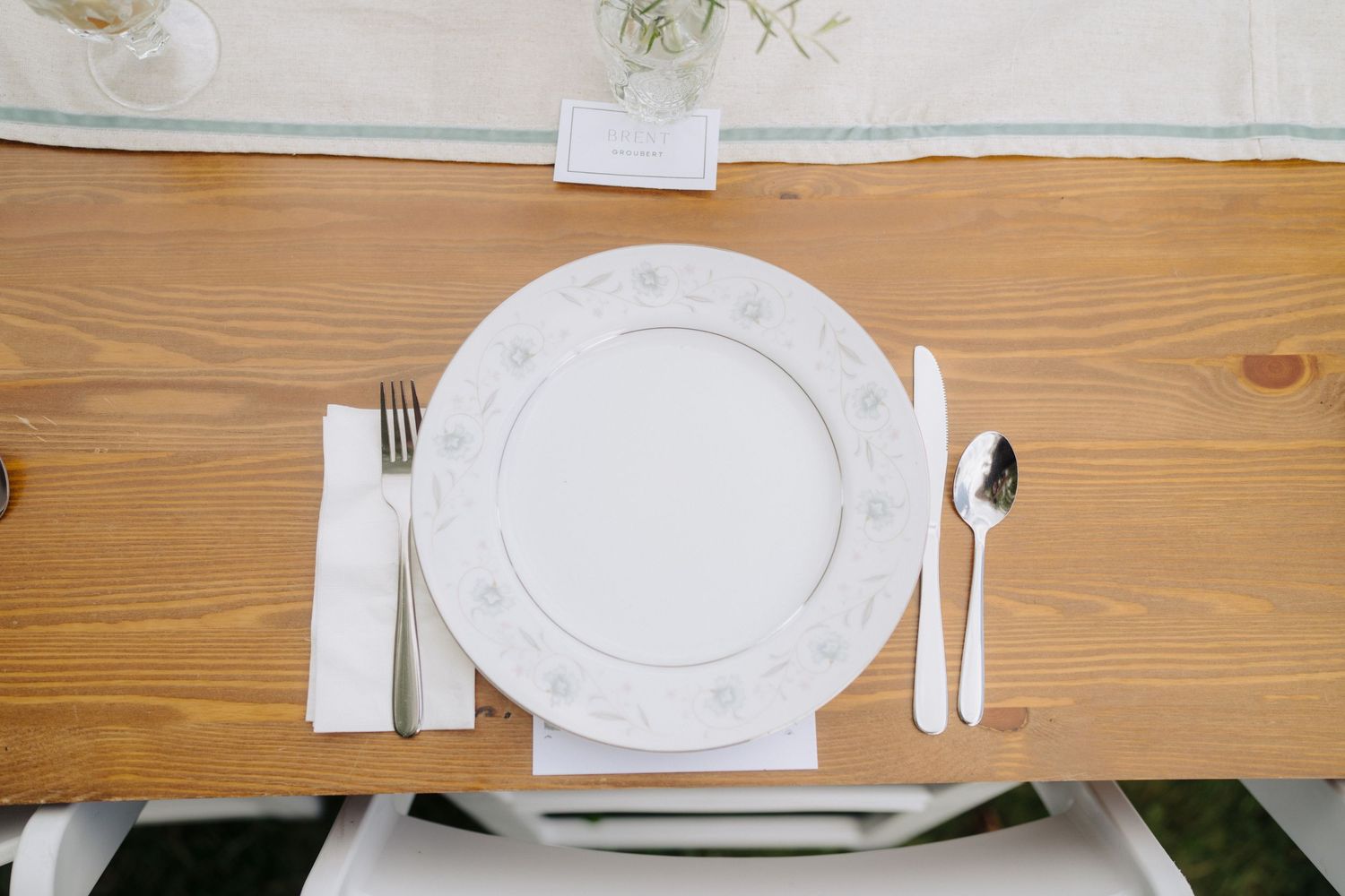 Minimalist table settings with white plates and linens on wooden tables at wedding reception.