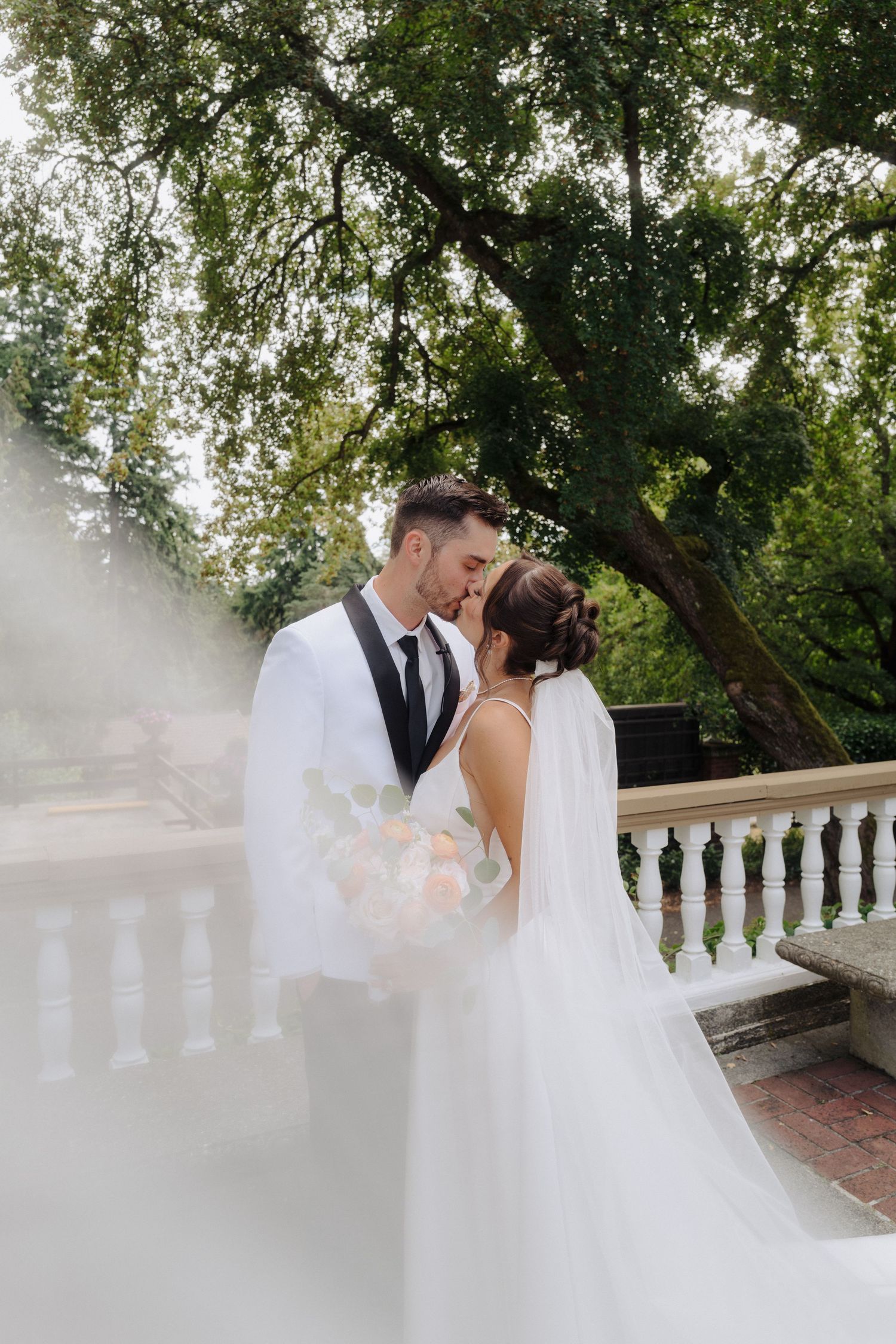 A romantic outdoor wedding portrait with white balustrade and trees in background.