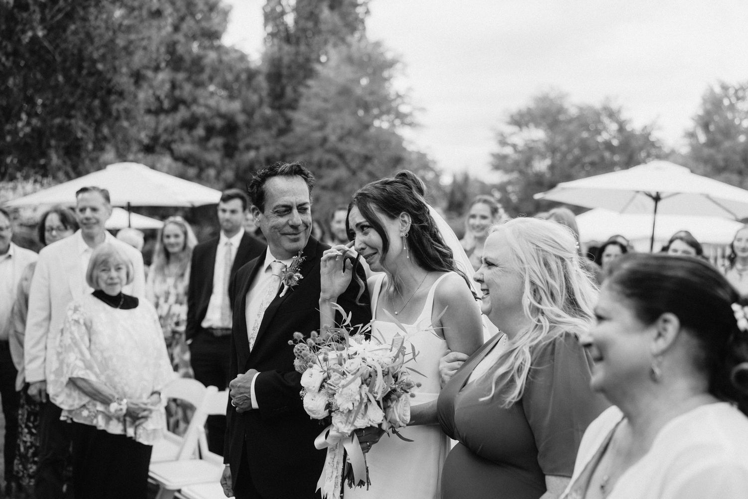 Black and white photo of wedding guests laughing and celebrating during an outdoor reception.