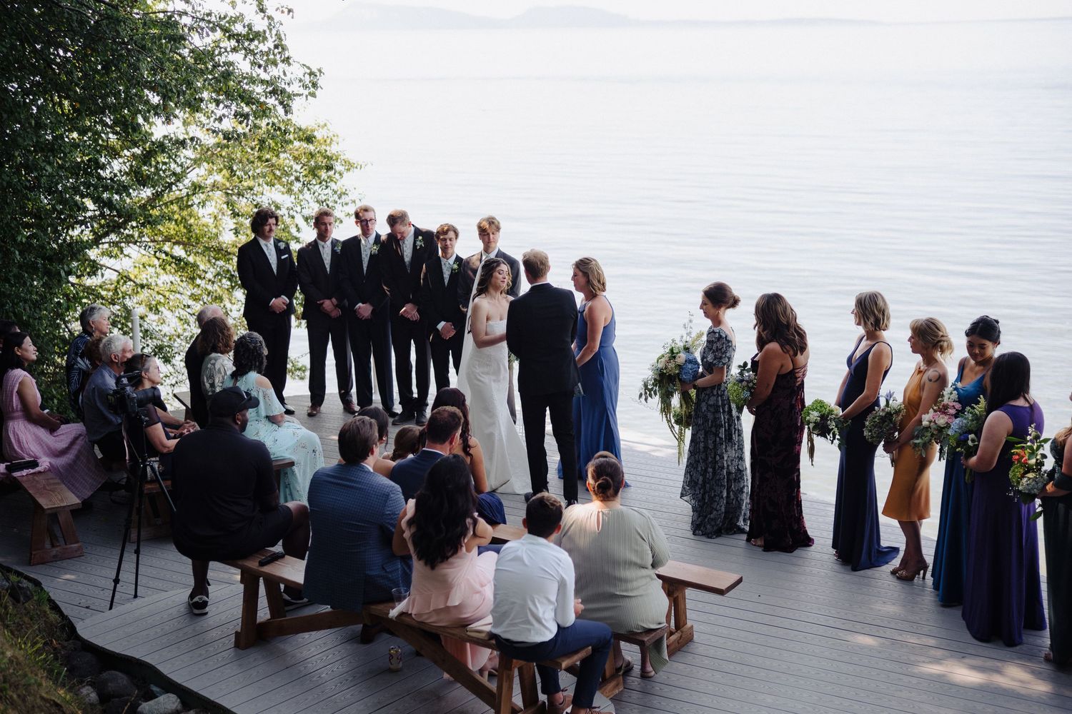 Wedding guests seated on a wooden deck overlooking a scenic waterfront view.