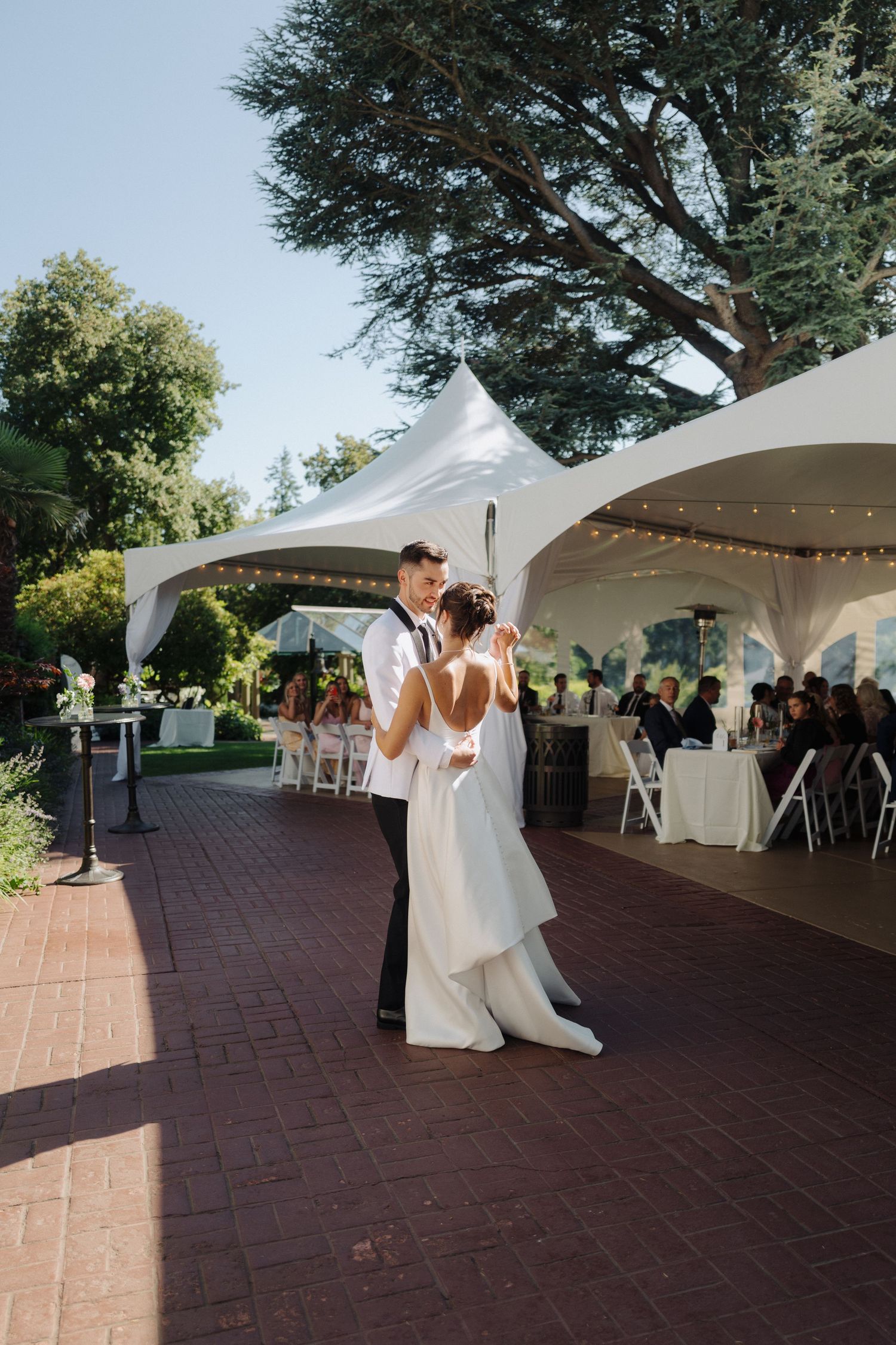 Couple sharing their first dance under white tent canopies at an outdoor wedding reception.