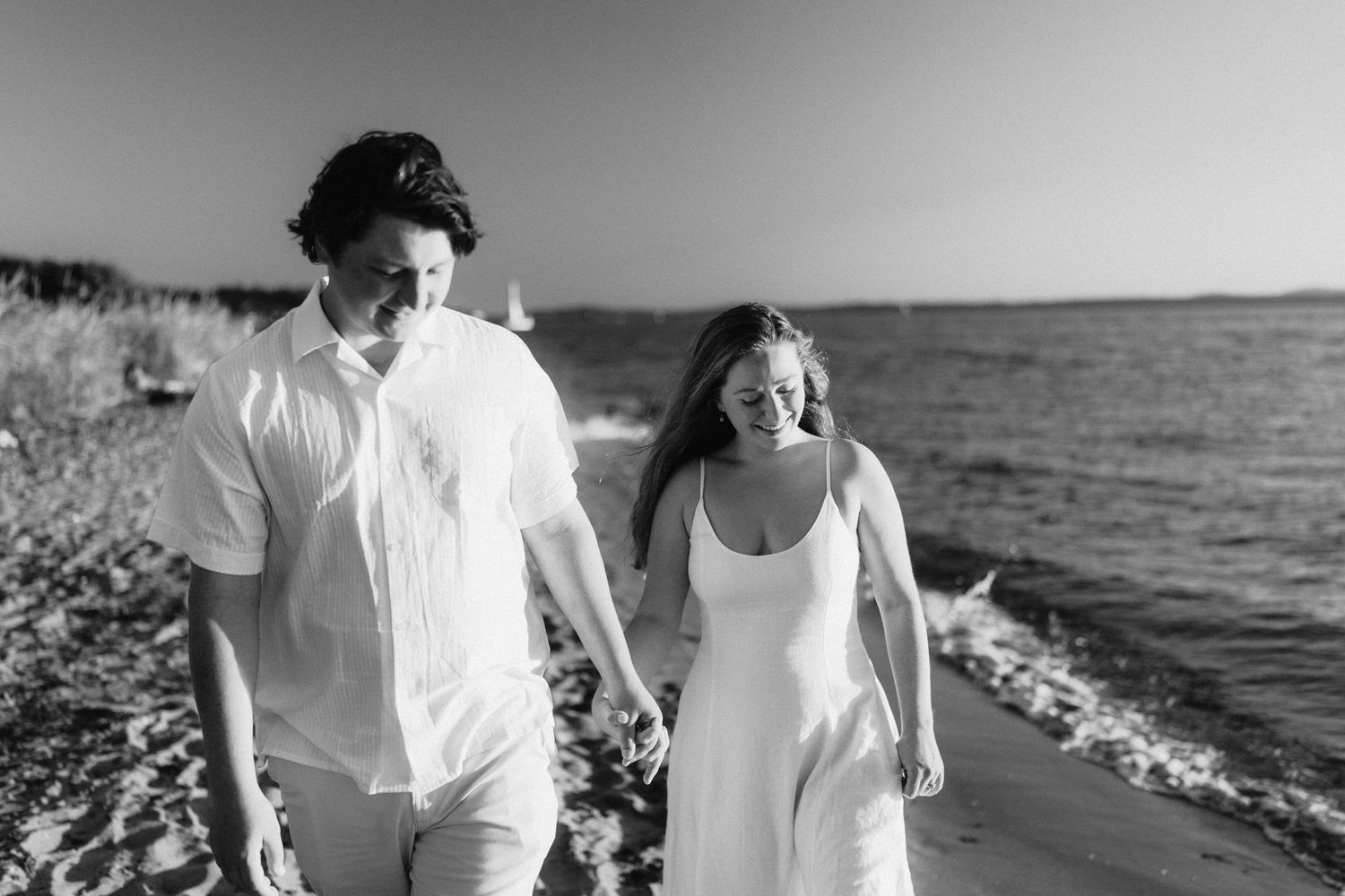 Couple walking hand in hand along a rocky beach shore with ocean views in monochrome style.