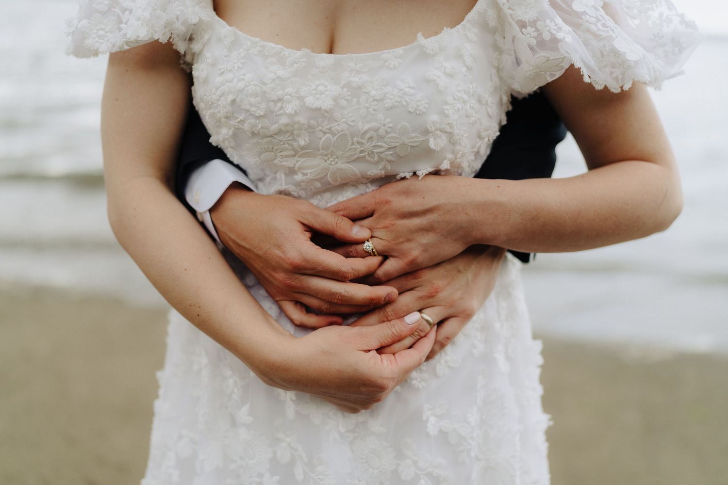 Detailed view of lace wedding dress with hands clasped at waist.