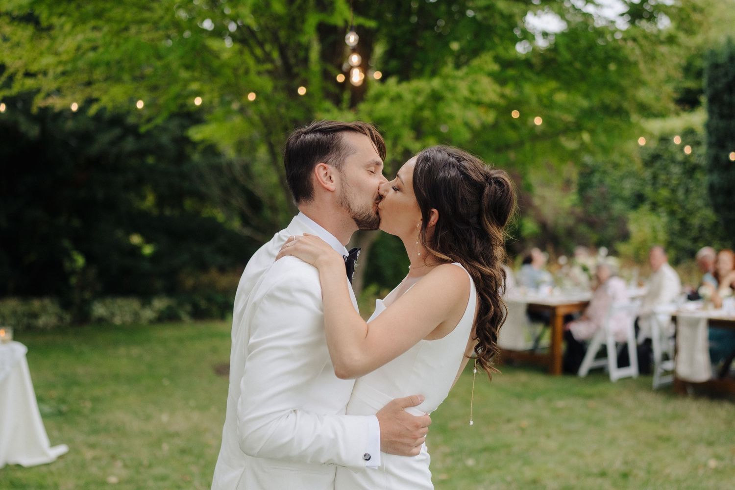 Outdoor evening wedding reception with string lights illuminating dancers on a grass lawn.