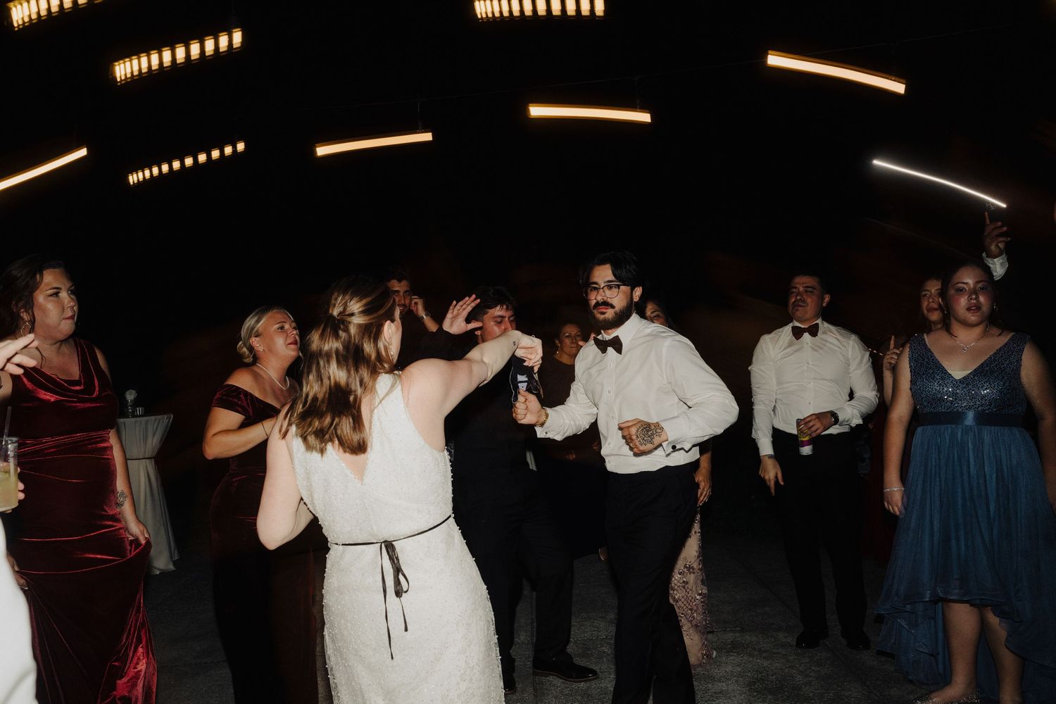 Wedding guests enjoying themselves on a dimly lit dance floor with string lights above.