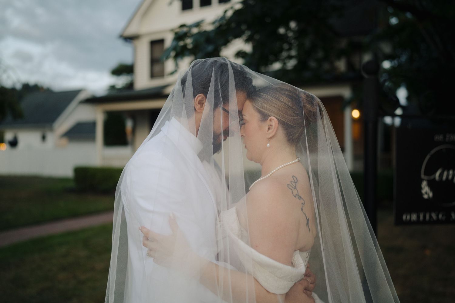 Romantic wedding couple shares an intimate moment under a flowing veil in an outdoor setting.
