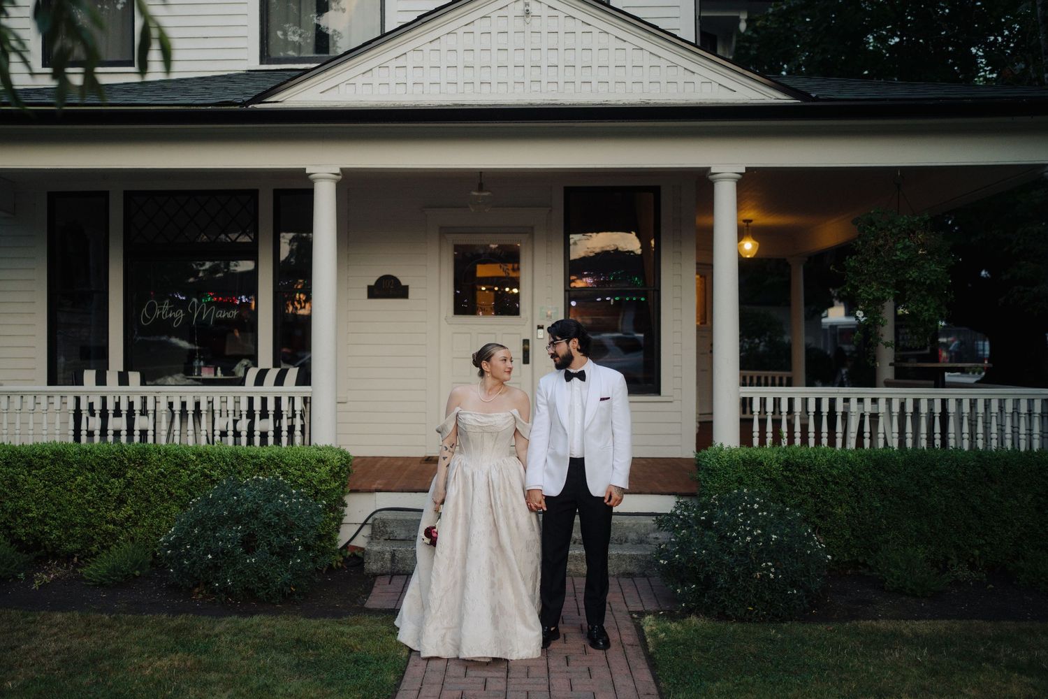 Elegant white farmhouse with wraparound porch serves as wedding venue backdrop.