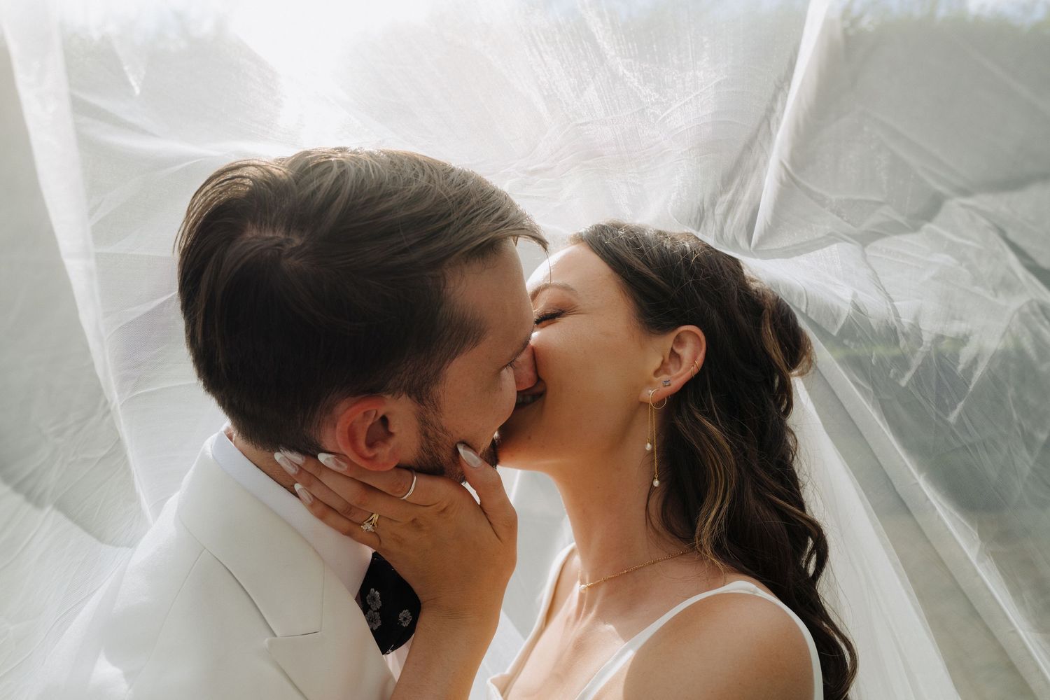 Romantic wedding moment captured through delicate white fabric in natural light.