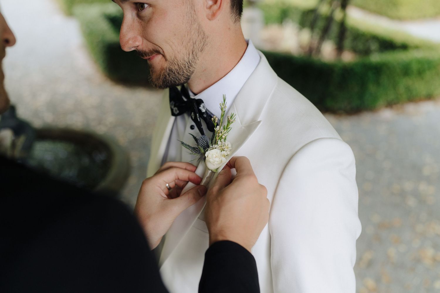 A couple shares a romantic moment in a wooded outdoor setting wearing elegant white wedding attire.