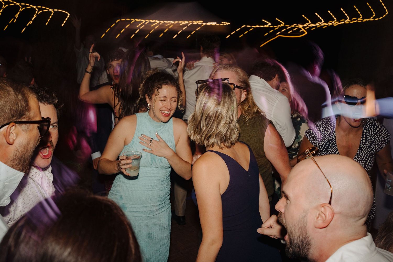 Wedding reception dance floor filled with guests celebrating under dim lighting.