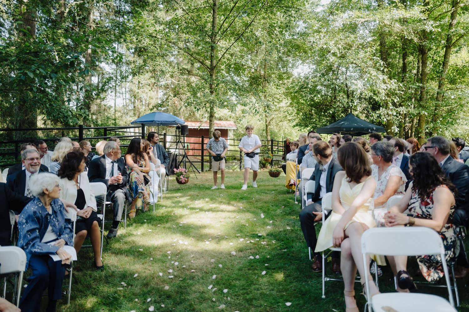 Outdoor wedding ceremony setup in a lush green garden with white chairs and guests gathered.
