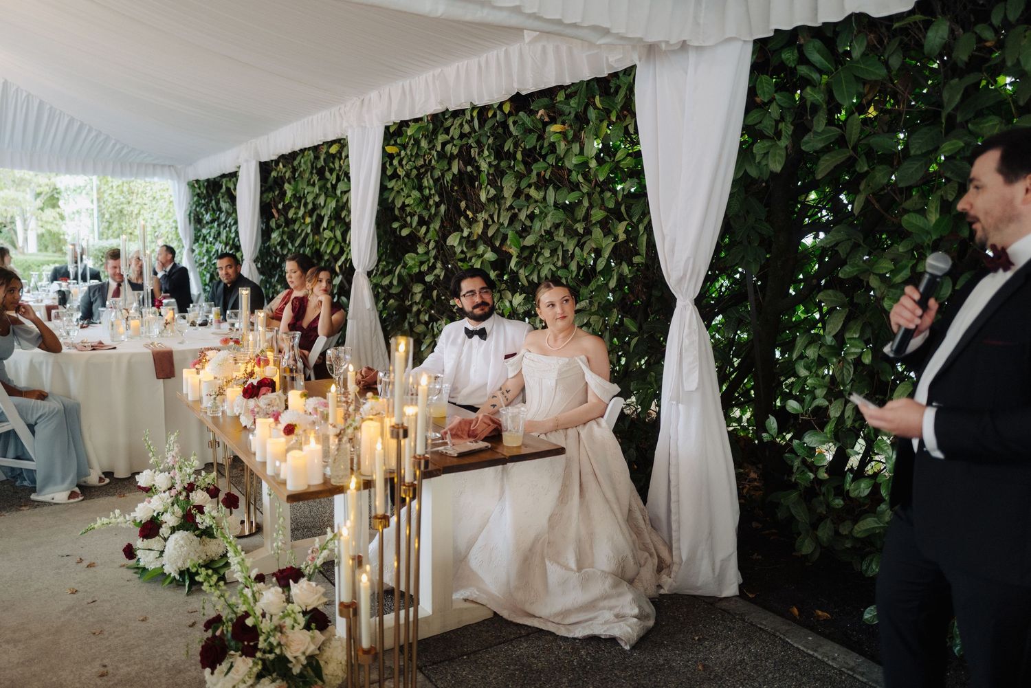 Elegant wedding reception setup with white draping, greenery walls and romantic lighting.