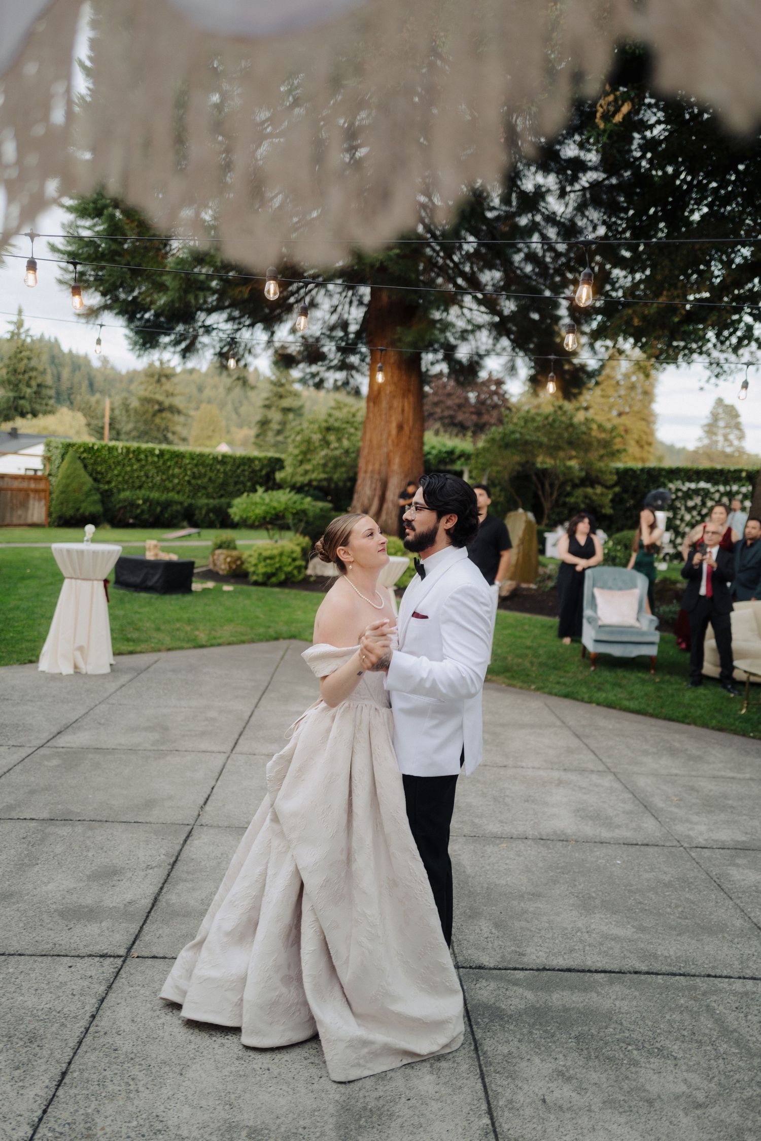 A couple shares their first dance on a concrete patio during an outdoor wedding celebration.